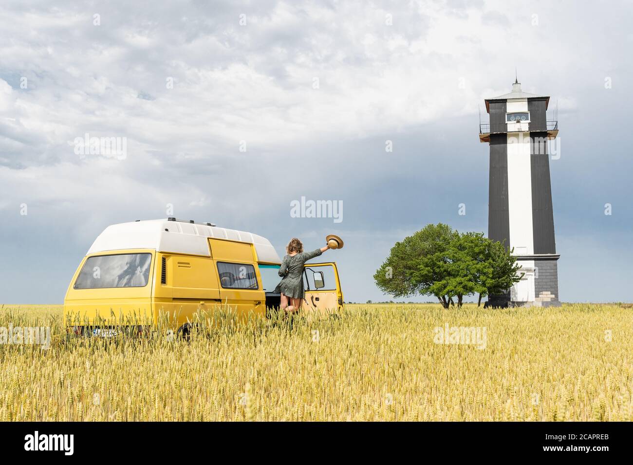 Giovane bionda che viaggia in un camper giallo attraverso la campagna. Motovedetta off-grid autocostruita. Stile country vintage. Foto Stock