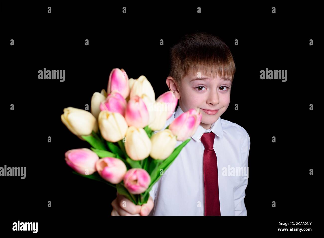 Il ragazzo carino in camicia bianca dà un bouquet di tulipani. Isolare su sfondo nero Foto Stock