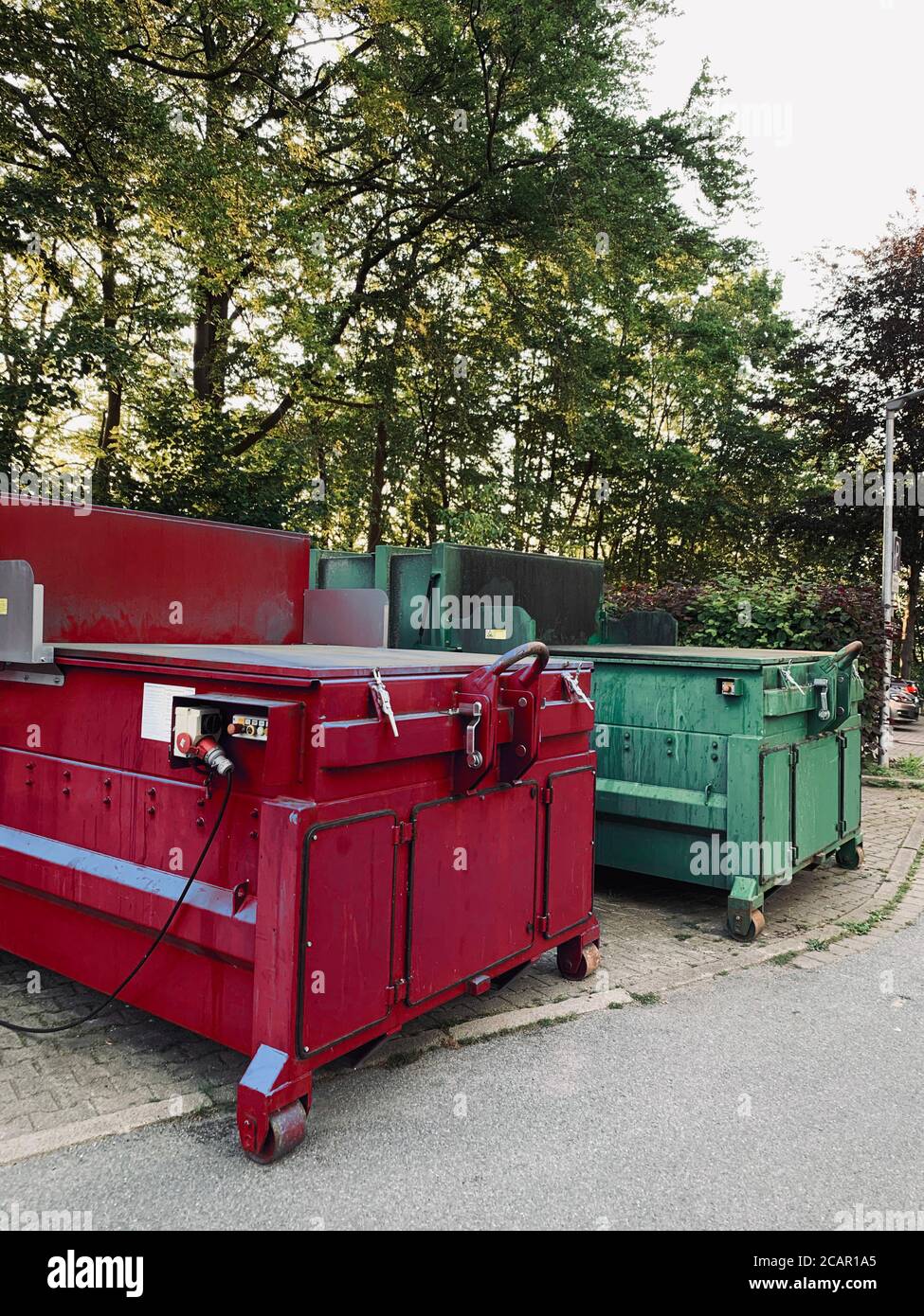in un sito industriale un compattatore per rifiuti verde e un il  compattatore per rifiuti rosso è affiancato Foto stock - Alamy