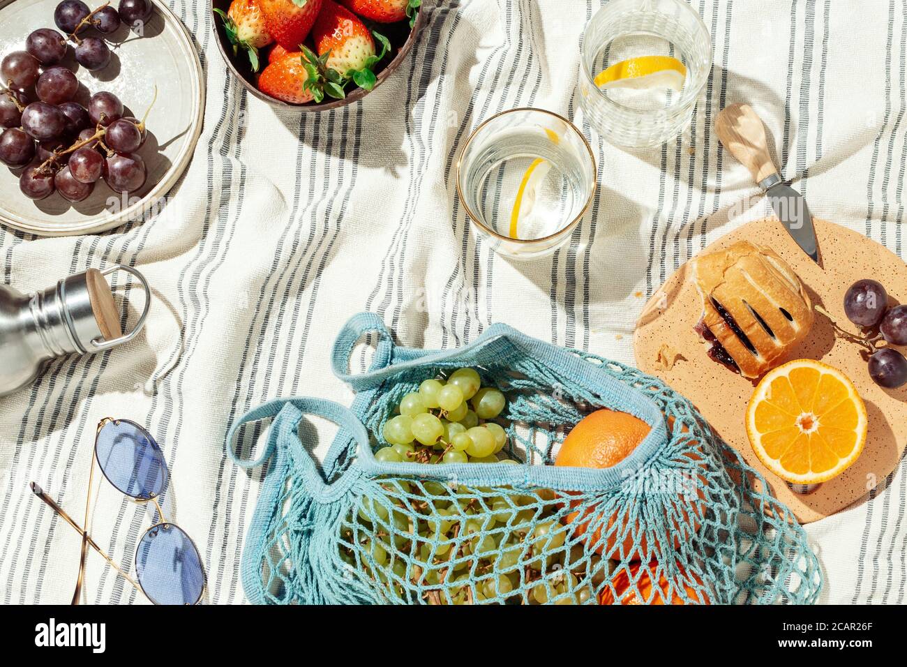 Estate pic-nic flatlay, frutta, frutti di bosco e acqua di limone su coperta di cotone a righe Foto Stock