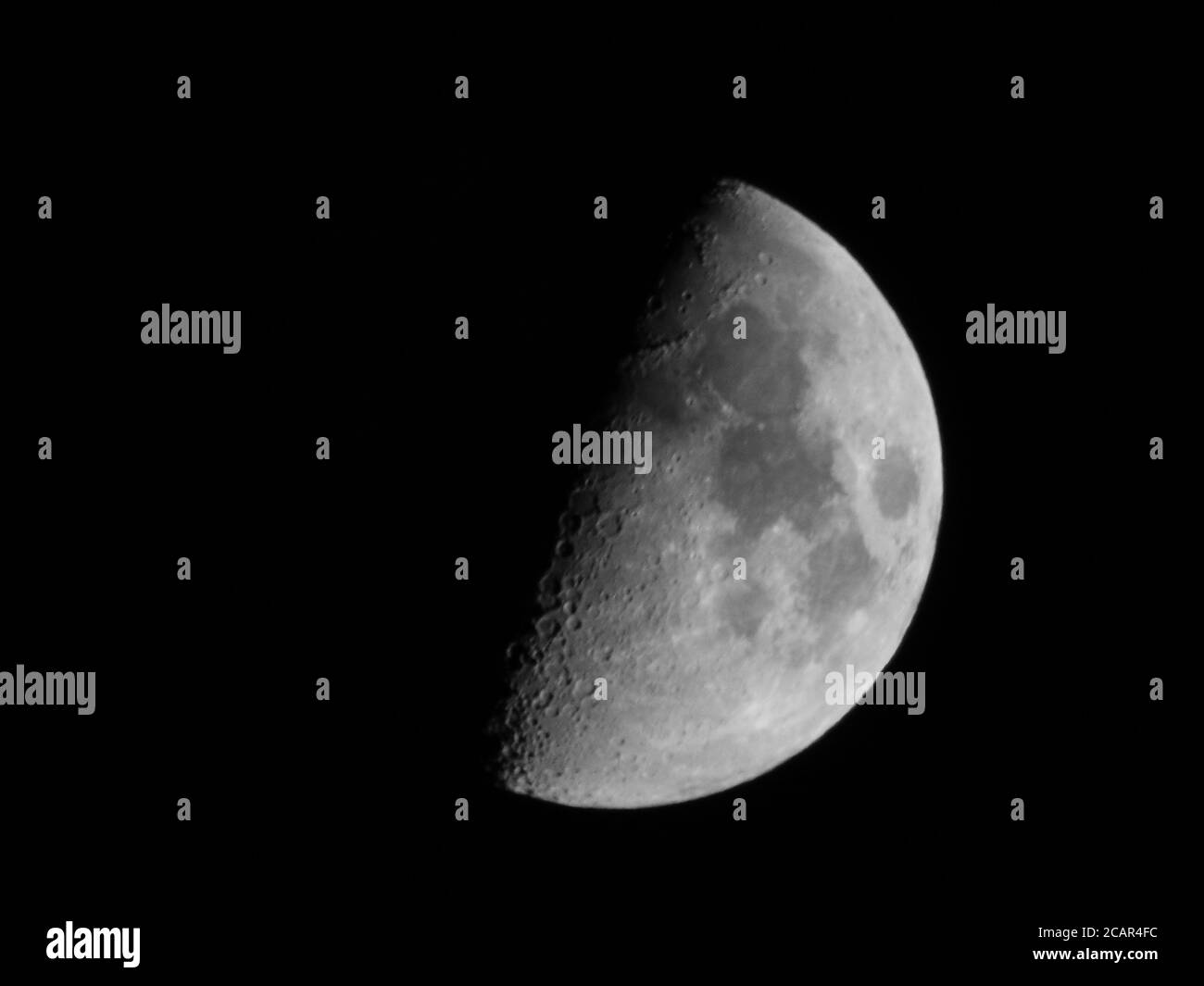 Il primo quarto di luna, conosciuto anche come mezzaluna, in bianco e nero, su uno sfondo di cielo nero Foto Stock