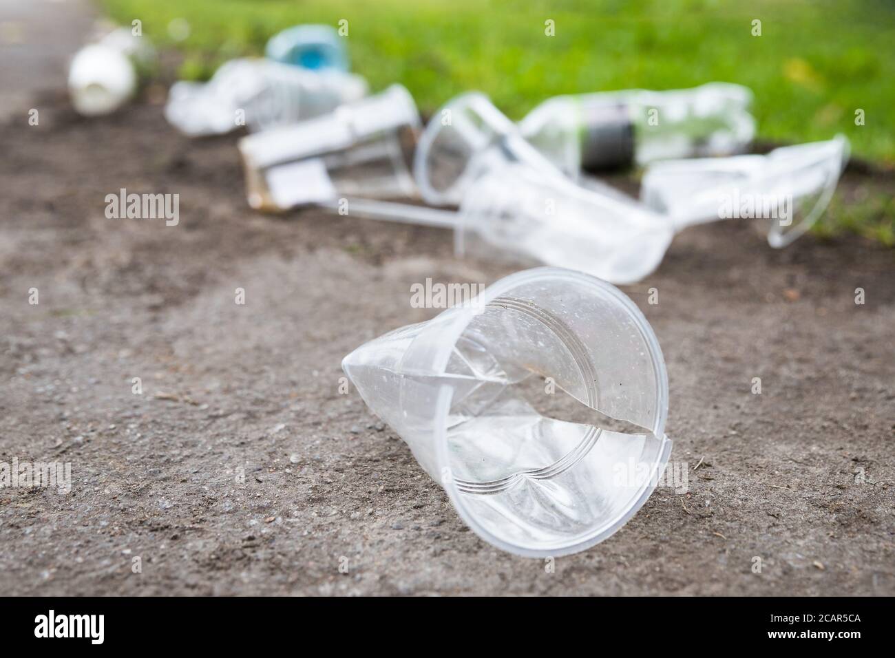 Cumulo di rifiuti sul percorso, primo piano. Svuotare le tazze di plastica usate e le bottiglie di plastica su sfondo sfocato, fuoco selettivo. Inquinamento ambientale Foto Stock