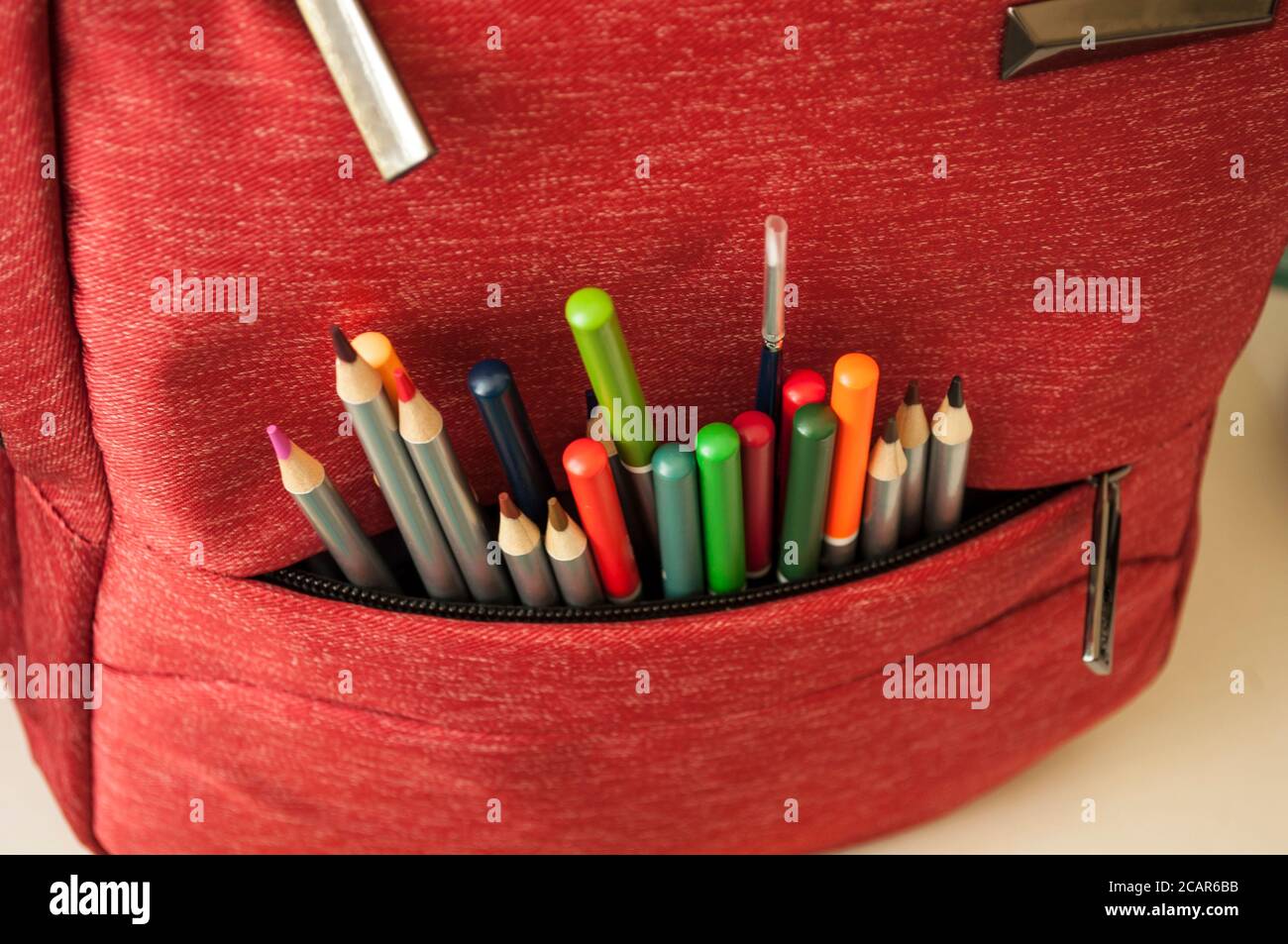 Matite colorate, un pennello guarda fuori da una tasca della borsa della scuola. Preparazione per la scuola. Foto Stock