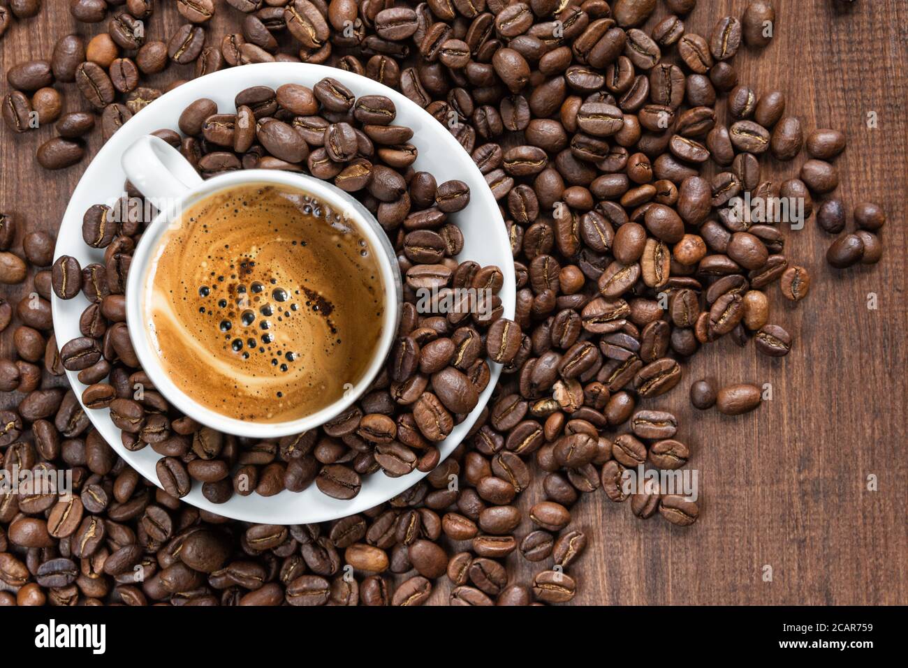 La tazza bianca di caffè in porcellana e i chicchi di caffè tostati sono sullo sfondo di legno, vista dall'alto Foto Stock
