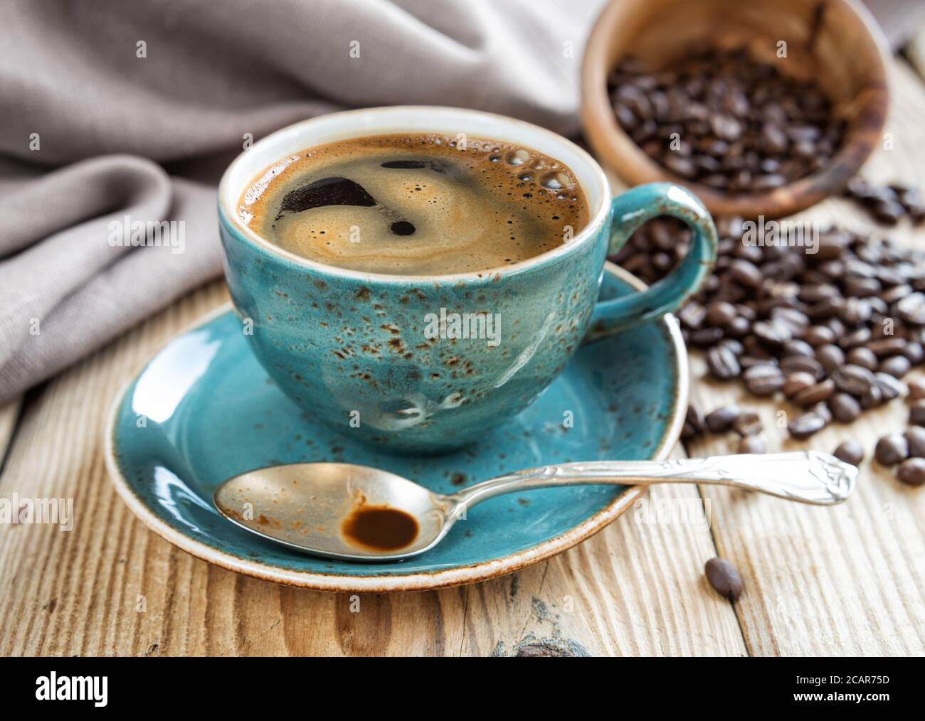 Tazza blu di caffè nero e chicchi di caffè sparsi uno sfondo di un panno di lino Foto Stock