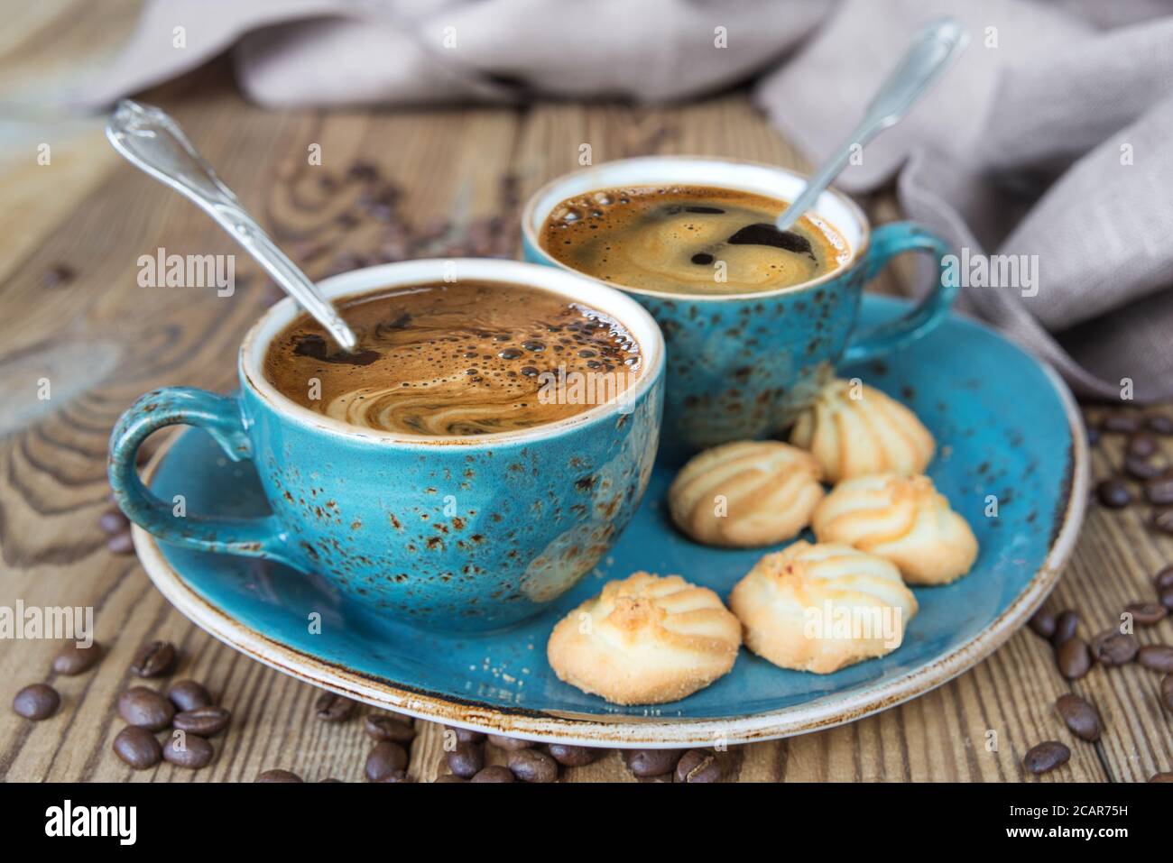 Due tazze blu di caffè nero, biscotti e tela di lino su vecchio tavolo di legno Foto Stock
