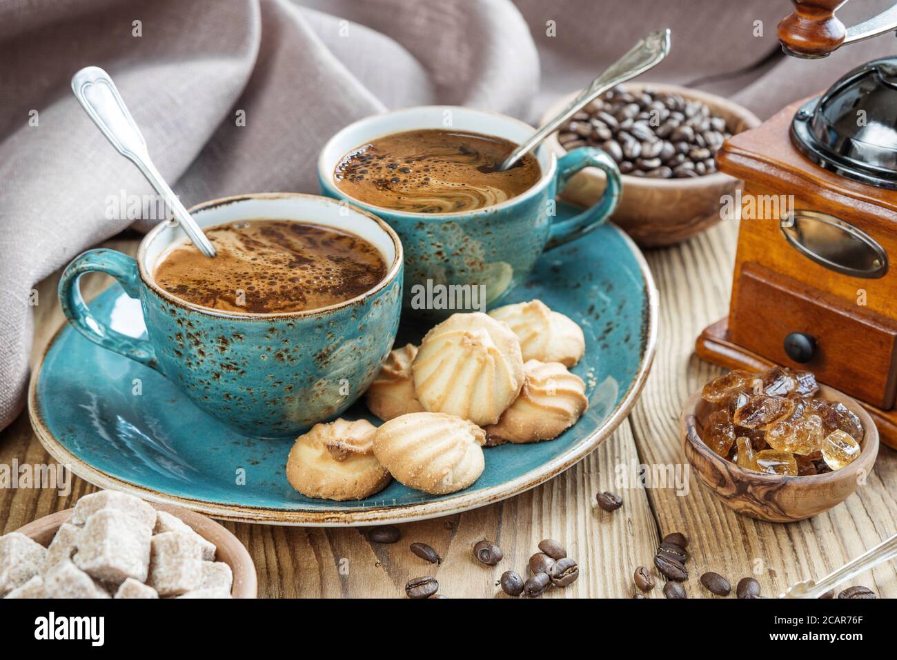 Blu di due tazze di caffè nero, cookie e pezzi di zucchero circondato da a scacchi in tela di lino e i chicchi di caffè sul vecchio tavolo in legno Foto Stock