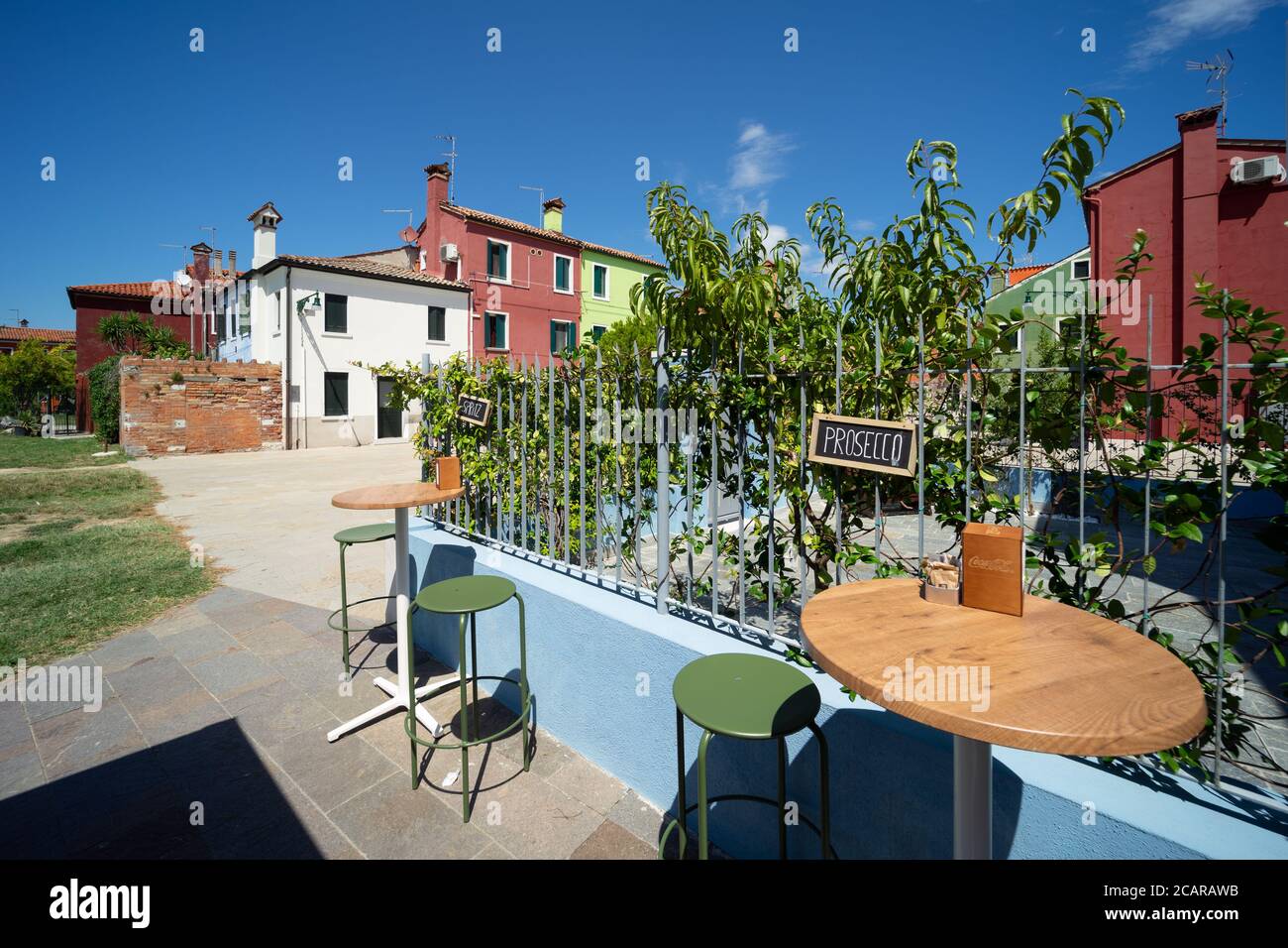 Isola di Burano, Laguna Veneziana, Venezia, Italia, un bar con terrazza all'aperto con spritz con le tradizionali case di villaggio colorate Foto Stock