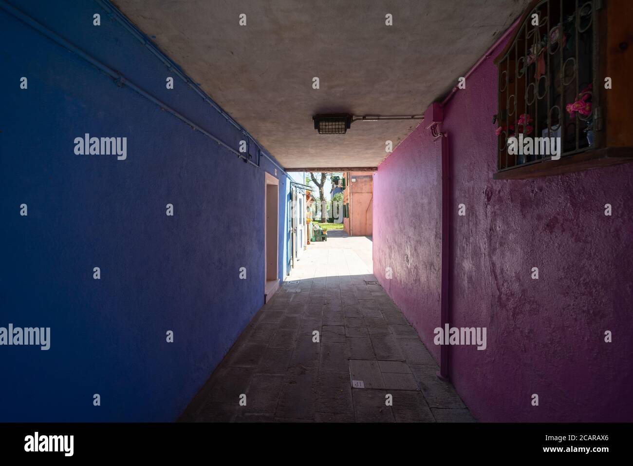 Isola di Burano, Laguna Veneziana, Venezia, Italia, uno stretto passaggio tra le tipiche case colorate e un effigie votivo nel centro della città Foto Stock