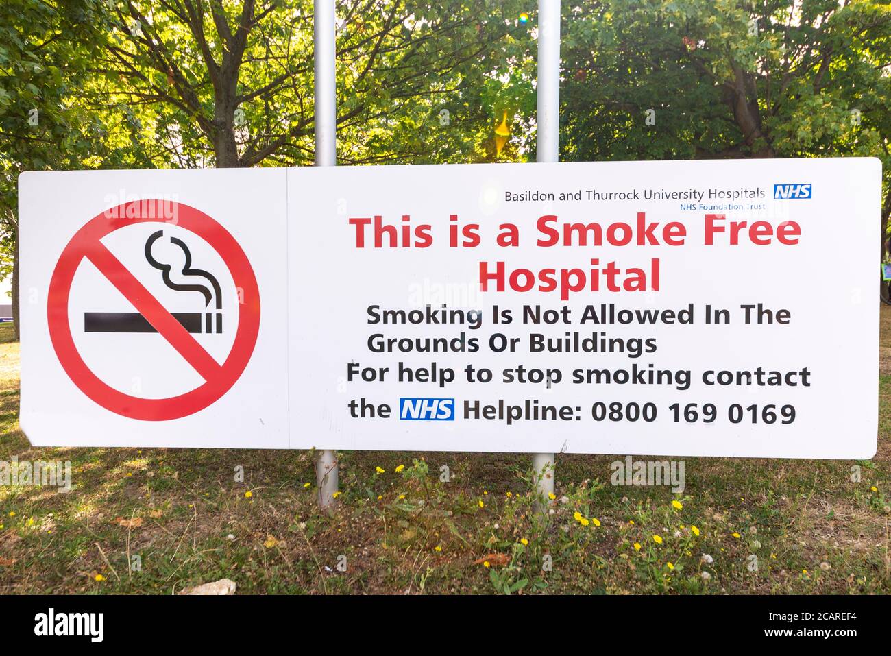 Cartello fuori dall'ospedale Basildon, Essex, Regno Unito. Questo è un ospedale non fumatori. Non è consentito fumare nei giardini o negli edifici. Non fumatori. Helpline NHS Foto Stock
