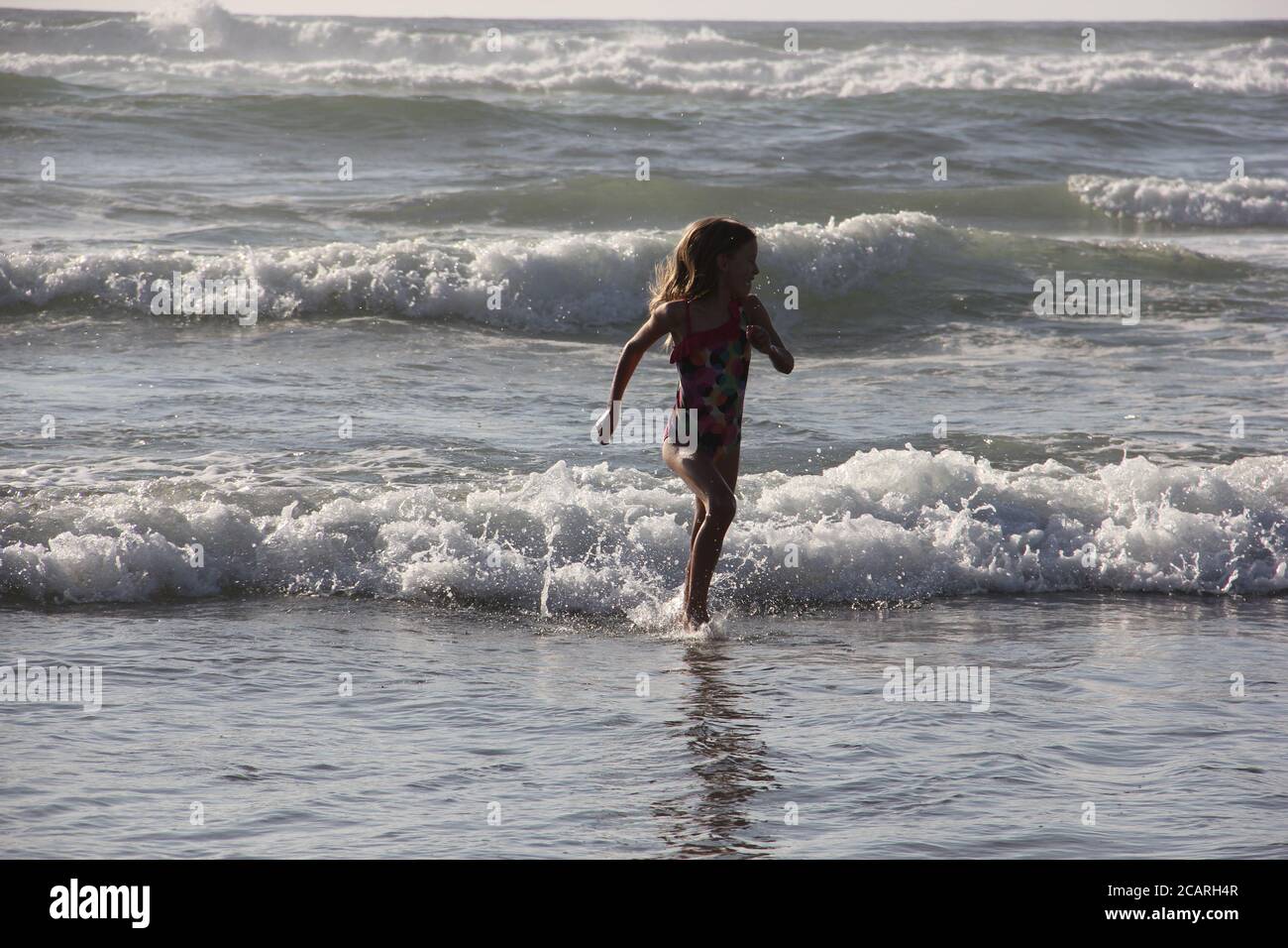 Le persone che si godono le onde della spiaggia durante le prime ore serali mentre il sole splende. Foto Stock