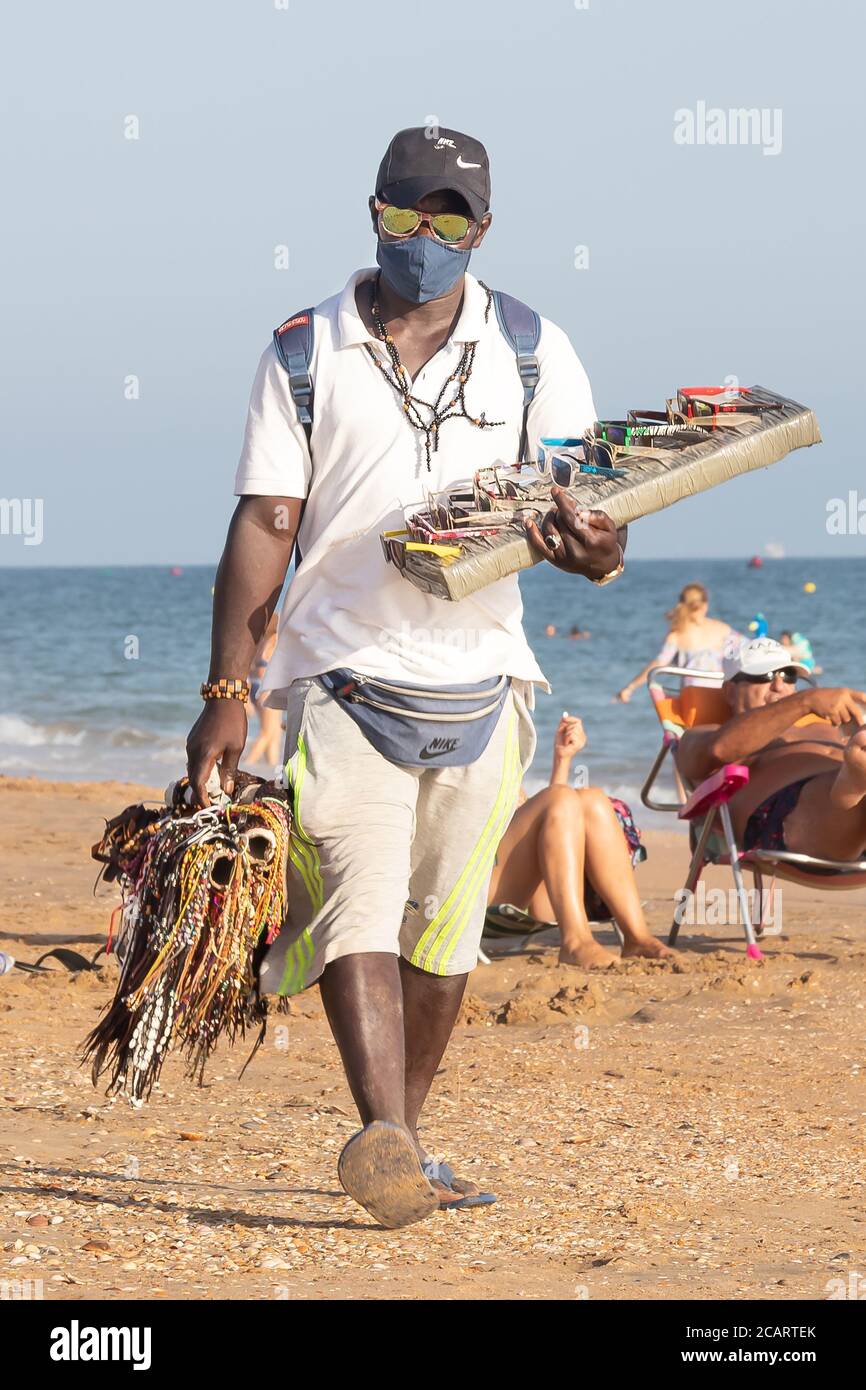 Punta Umbria, Huelva, Spagna - 7 agosto 2020: Immigranti africani che vendono i loro articoli sulla spiaggia indossando maschera protettiva o medica. Tutti i beni di Foto Stock