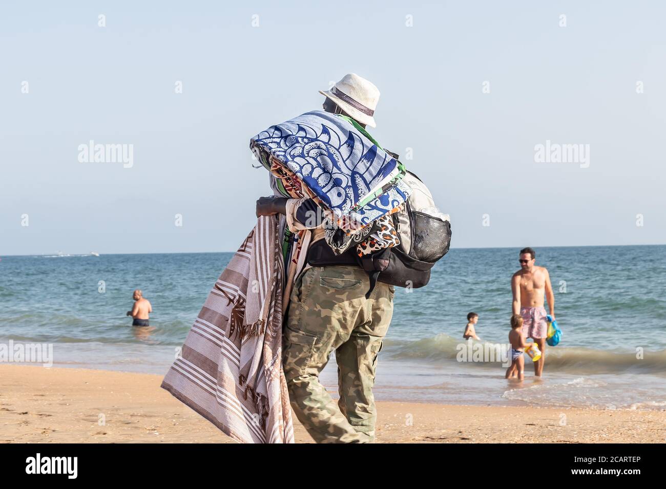 Punta Umbria, Huelva, Spagna - 7 agosto 2020: Immigranti africani che vendono i loro articoli sulla spiaggia indossando maschera protettiva o medica. Tutti i beni di Foto Stock