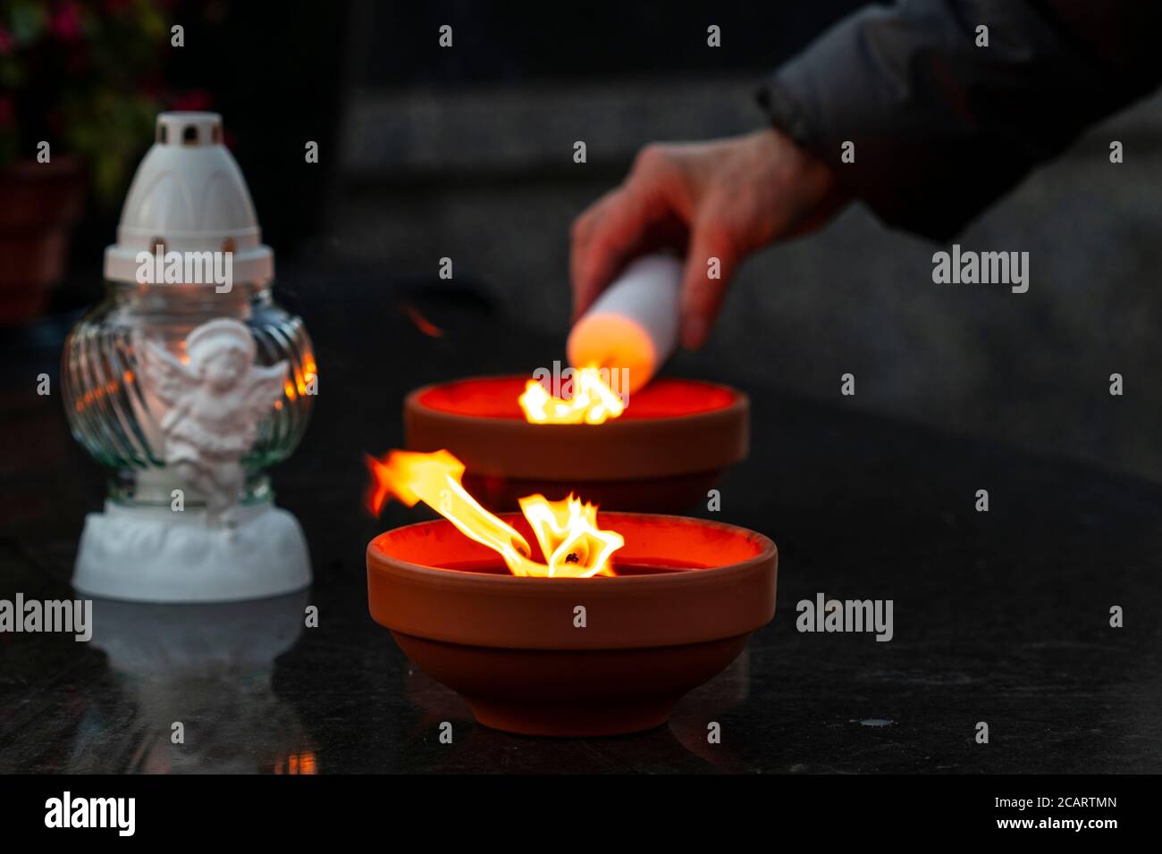Tradizionali candele di tomba bruciante su una tomba durante tutte le anime' Giorno in sfondo vecchia mano donna che spara la candela Foto Stock