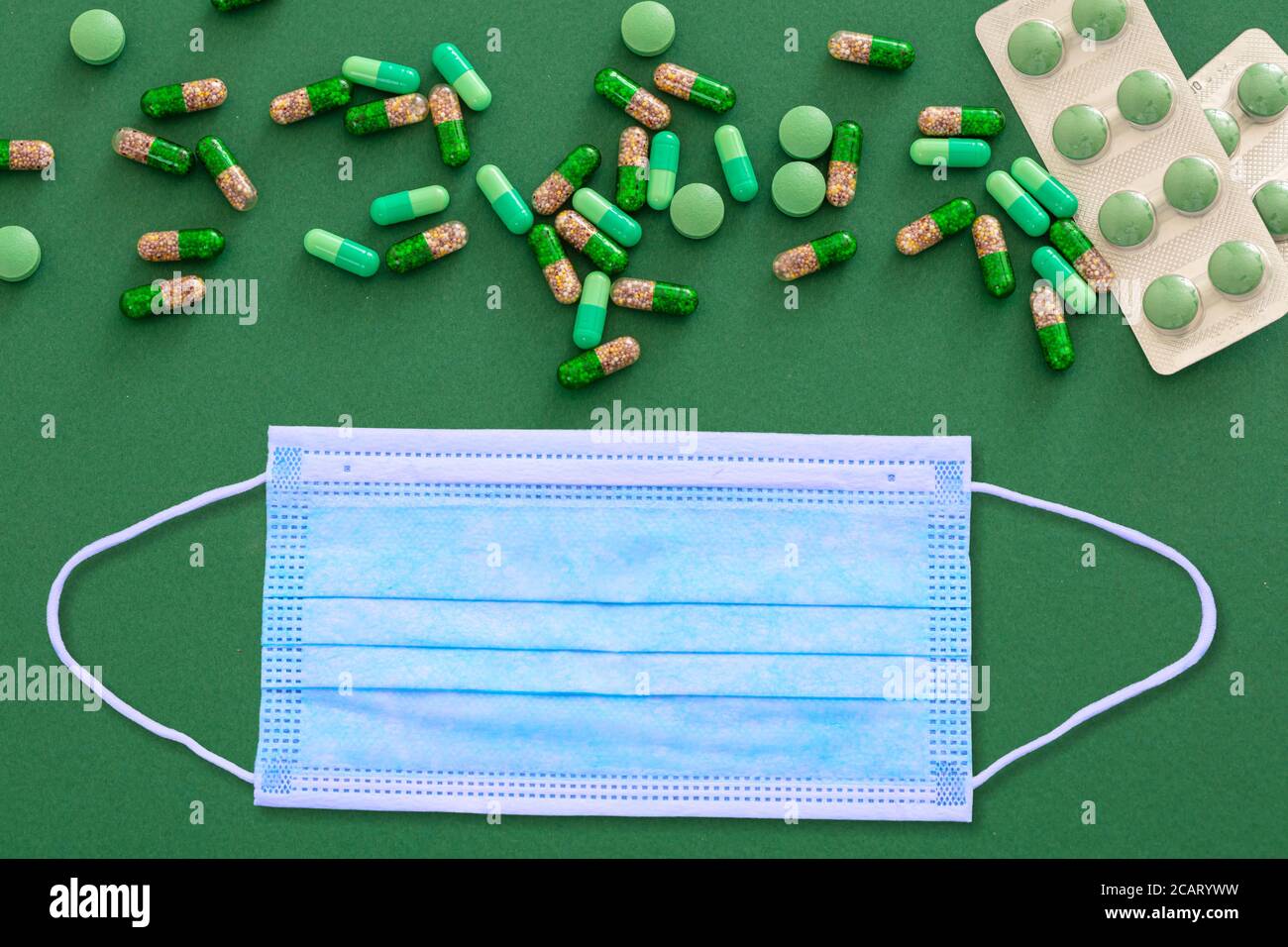 Coronavirus e medicazione piatto posare. Maschera protettiva e pillole di medicina su sfondo verde, vista dall'alto, spazio di copia Foto Stock