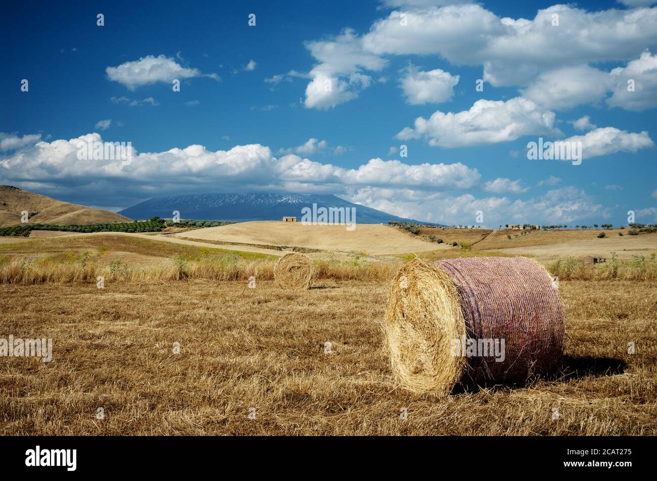Paesaggio rurale della Sicilia in estate con balle di fieno rotonde e abbandonato edificio su una collina sotto il cielo blu e. nuvole bianche Foto Stock
