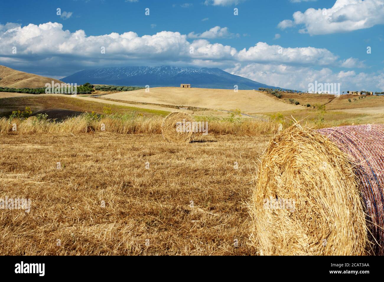 Paesaggio rurale della Sicilia in estate con balle di fieno rotonde e abbandonato edificio su una collina sotto il cielo blu e. nuvole bianche Foto Stock