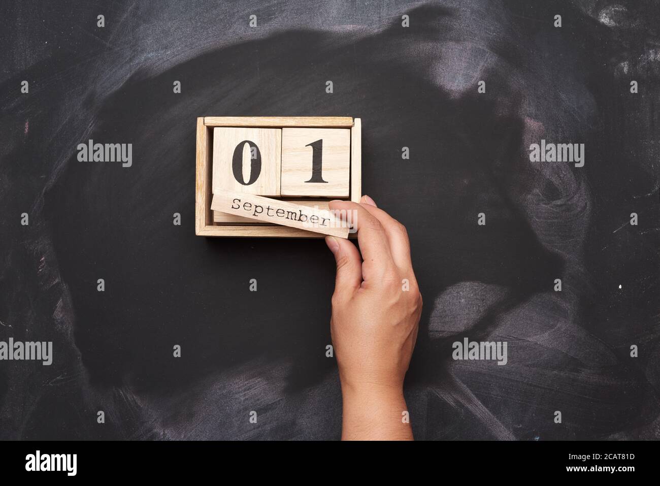 calendario in legno con data 1 settembre e mano femminile, sfondo in gesso nero, ritorno a scuola Foto Stock