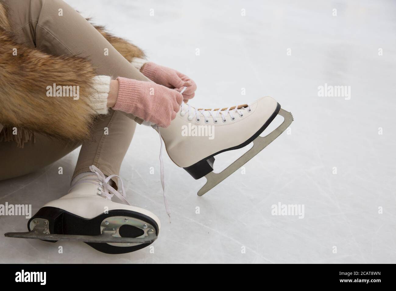 Closeup di donna in pelliccia cappotto e guanti rosa che indossano Pattini bianchi su pista di ghiaccio in inverno day.Woman legando skates.Weekends attività all'aperto in inverno Foto Stock