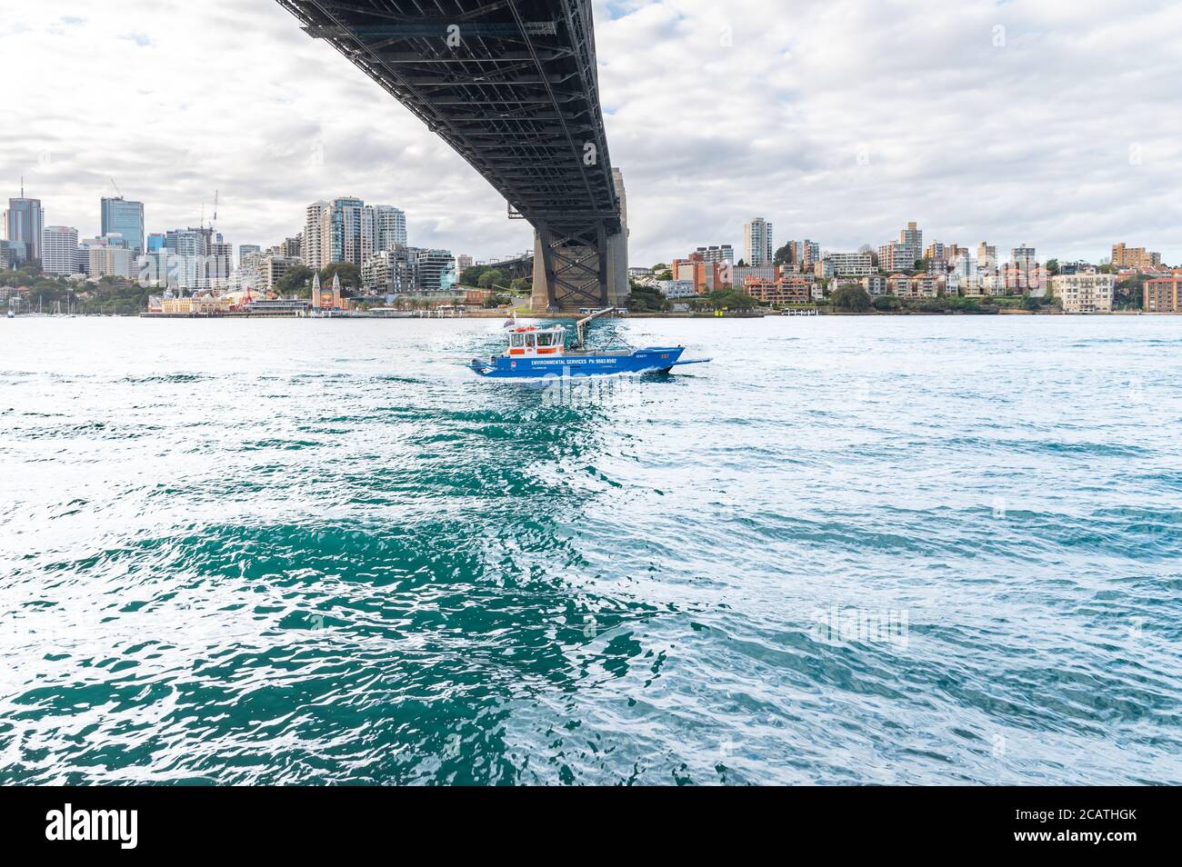 Ambiente servizi Barca vela sotto Sydney Harbour Bridge struttura ON un pomeriggio invernale nuvoloso Foto Stock
