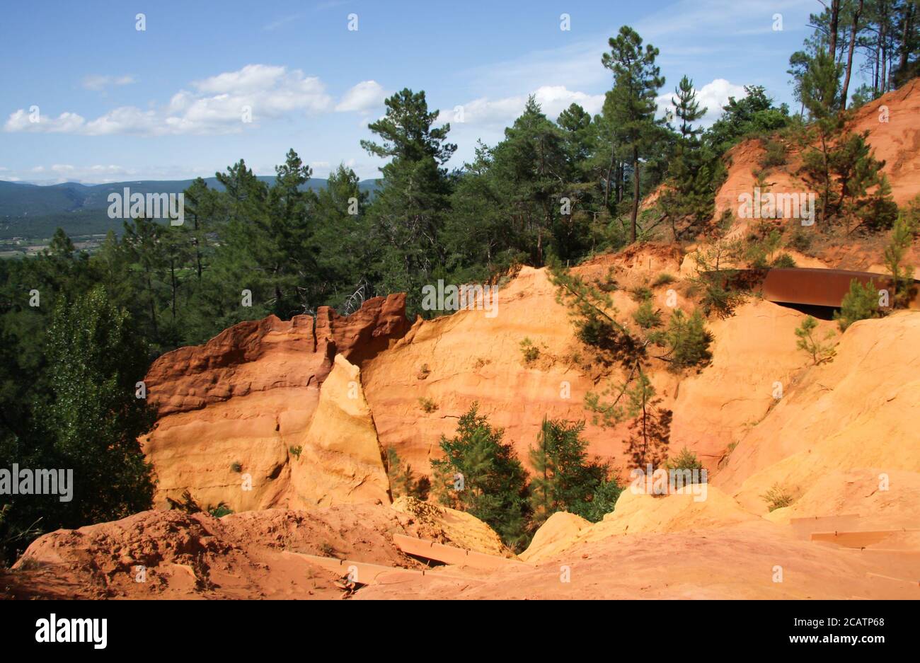 Vista delle colorate scogliere color arancio ocra con pini e cielo blu al parco naturale regionale di Roussillon, Vaucluse, Luberon, Francia Foto Stock