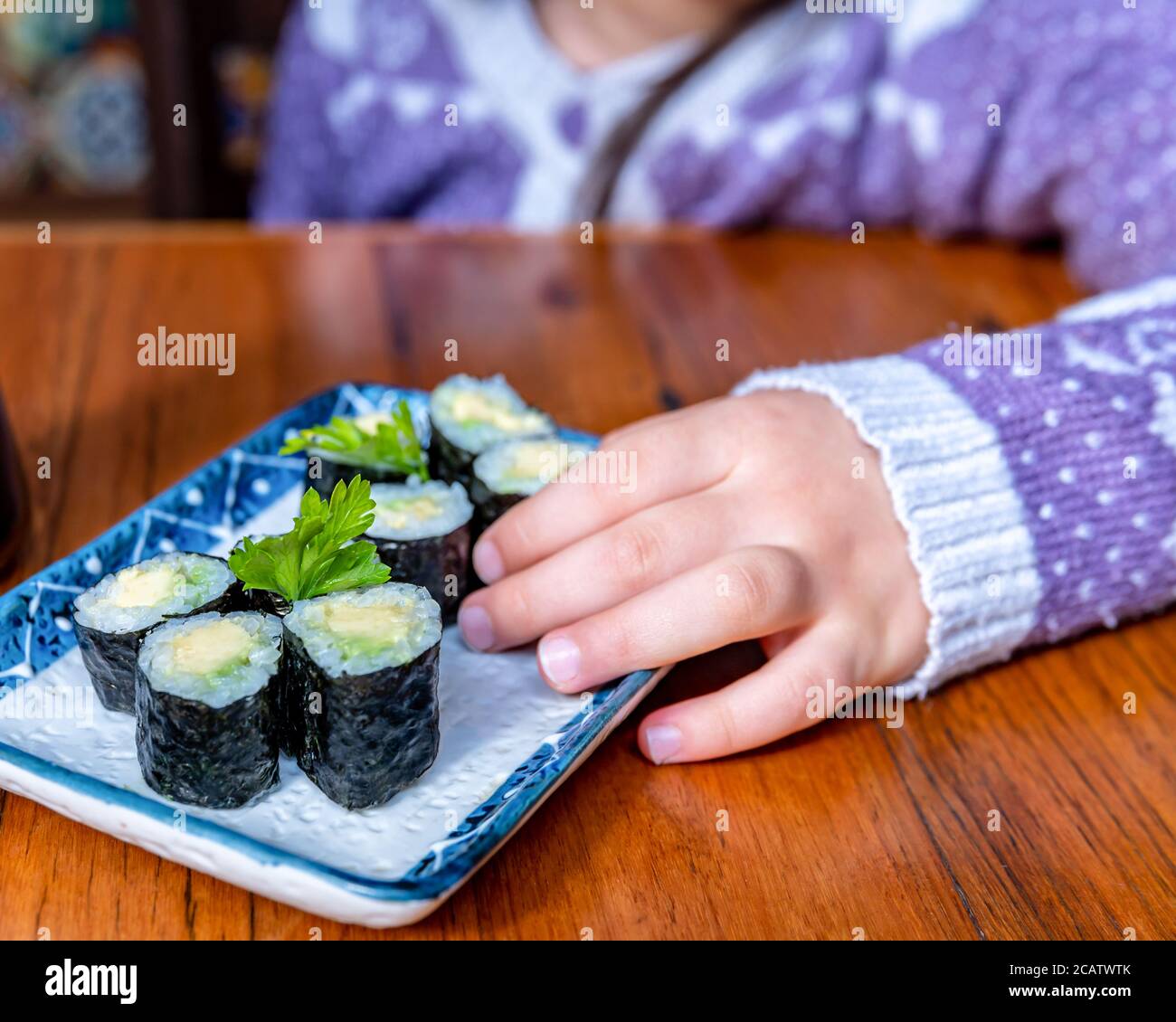 Mini avocado Sushi Rolls e una ragazza che ne tiene uno Foto Stock