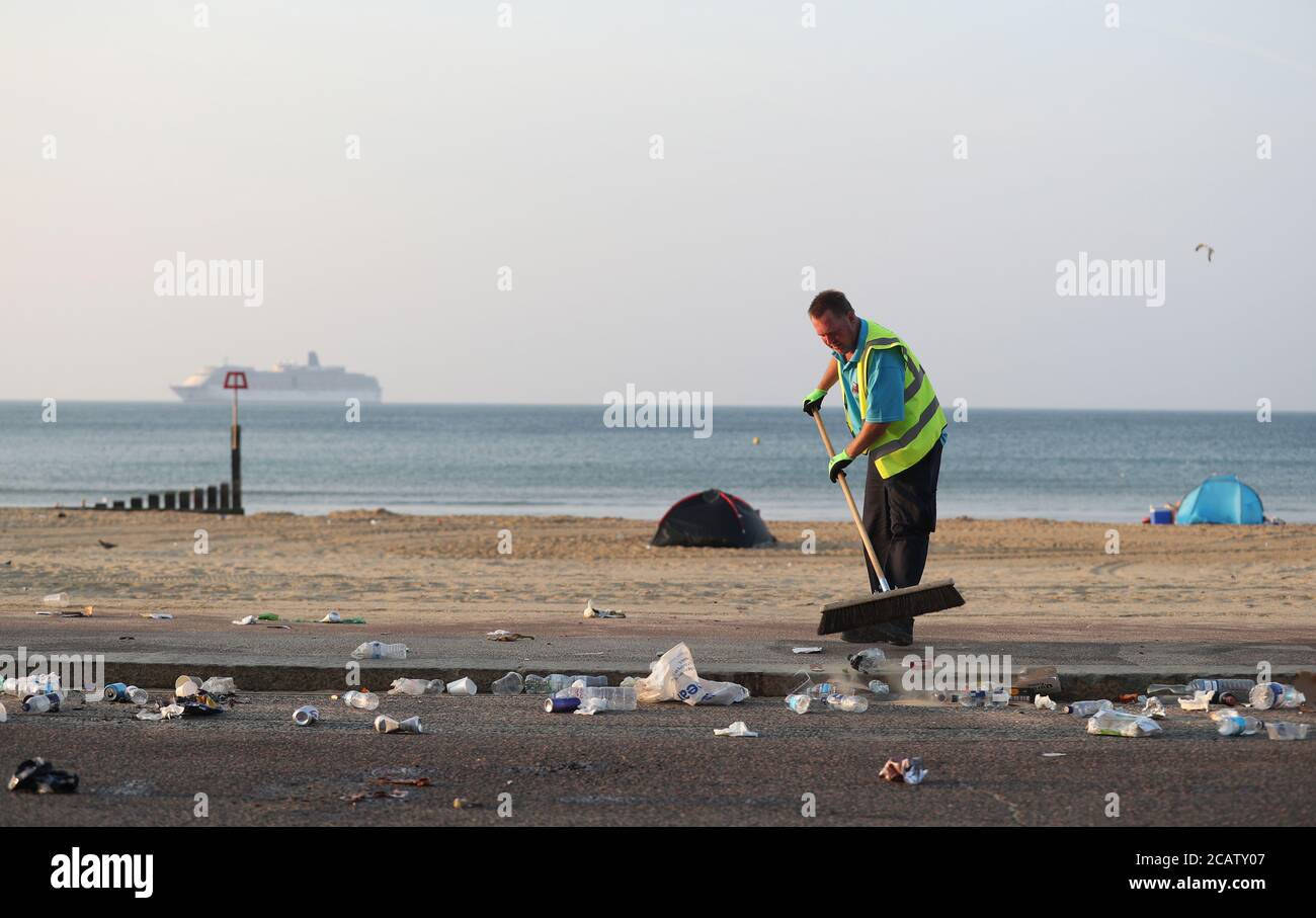 Un membro del consiglio del BCP spazza in su i rifiuti eccedenti che sono caduti dai bidoni che sono stati svuotati sulla spiaggia di Bournemouth in Dorset. Foto Stock
