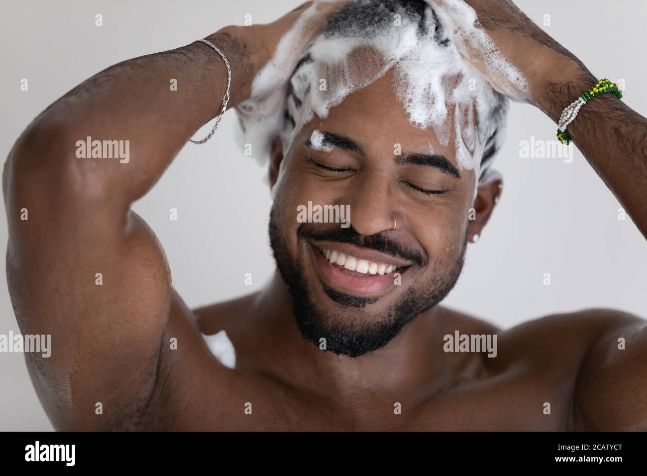 Primo piano sorridente afroamericano che lava i capelli con shampoo Foto Stock