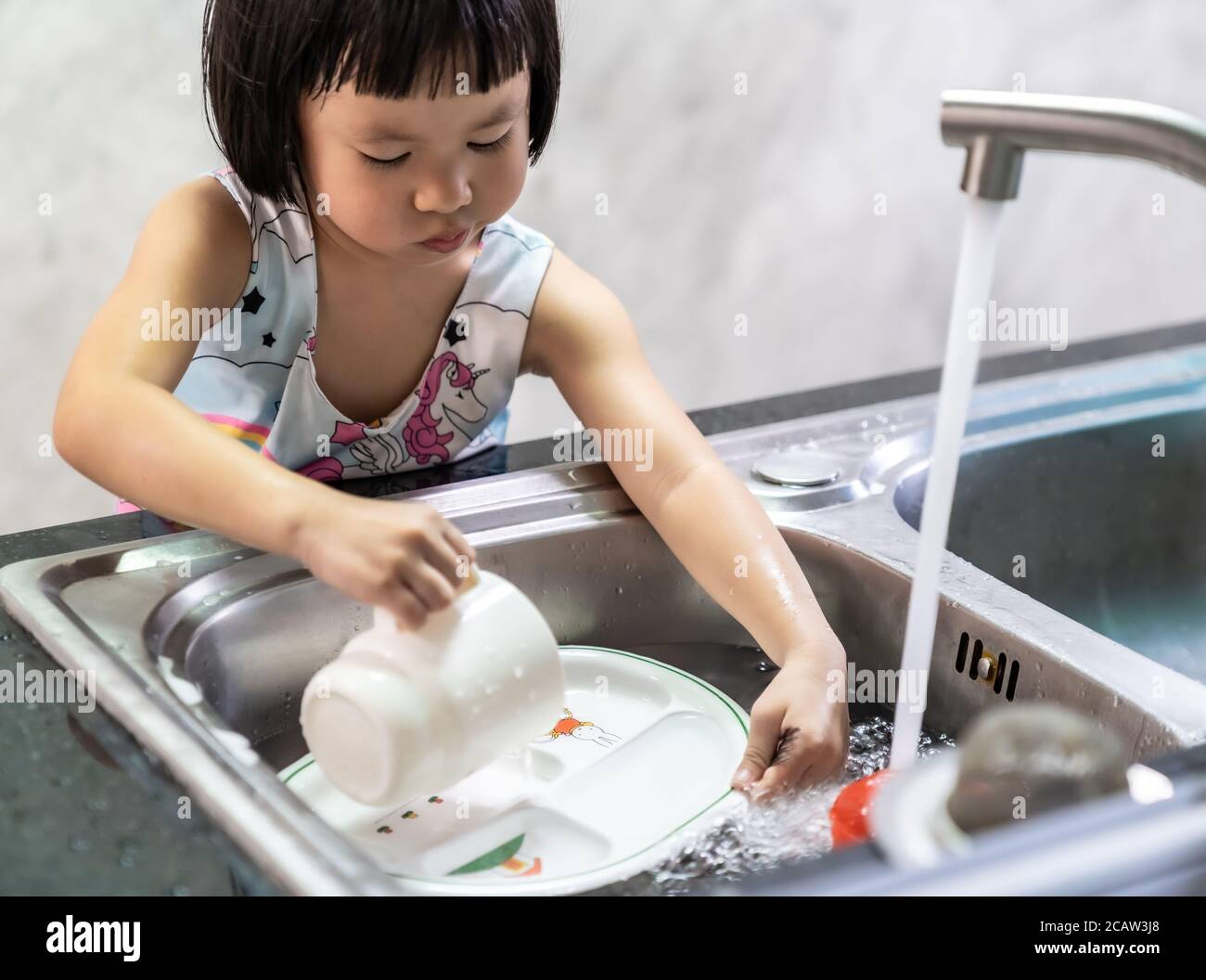 Ragazza asiatica lavando il suo piatto e stoviglie da lei stessa, casalinghi per il bambino fare la funzione esecutiva per il capretto. Lavoro di casa per lo stile di vita dei bambini e la famiglia Foto Stock