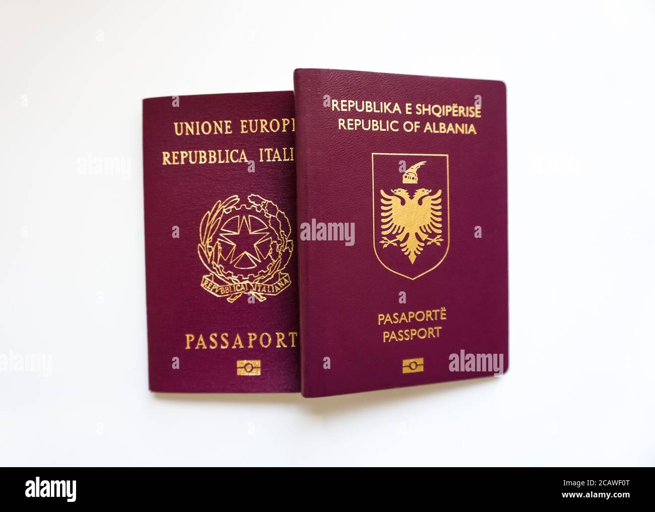 Tenendo in mano due passaporti di nazionalità diversa su sfondo bianco - Albania e Italia - imbarco, treveling e documenti Foto Stock