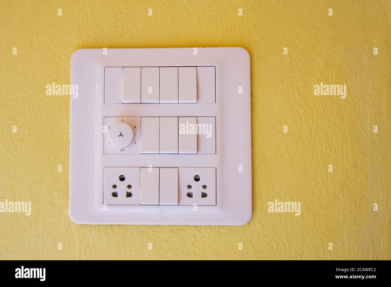 un moderno interruttore di illuminazione elettrica, un dimmer e un pannello di uscita isolati sulla parete gialla Foto Stock
