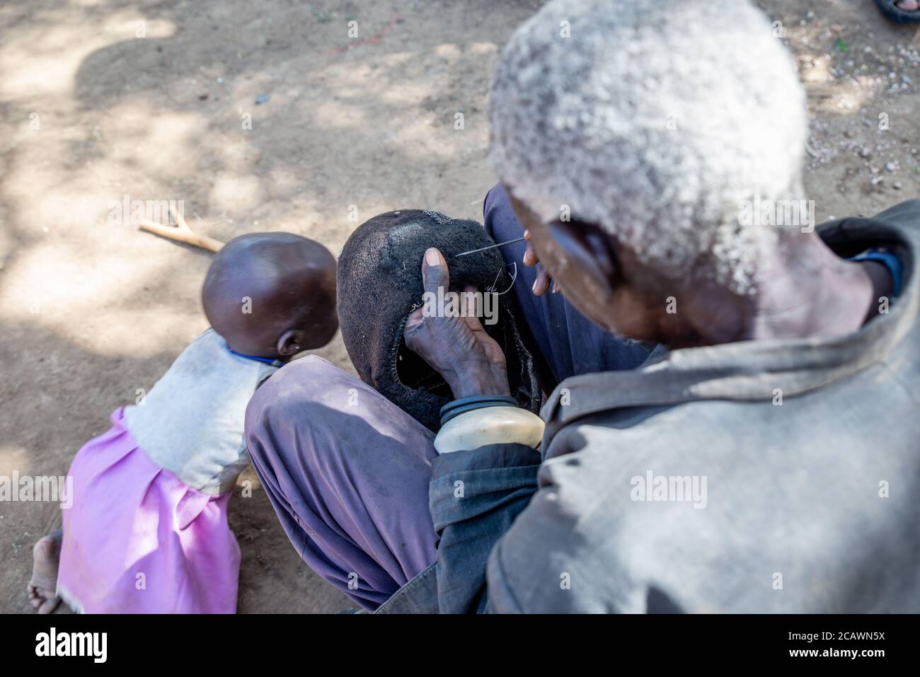 Vecchio uomo Karamejong mantenendo un hdeaddress etimat (epukot) fatto di capelli umani e piume di struzzo, distretto di Moroto, Uganda Foto Stock