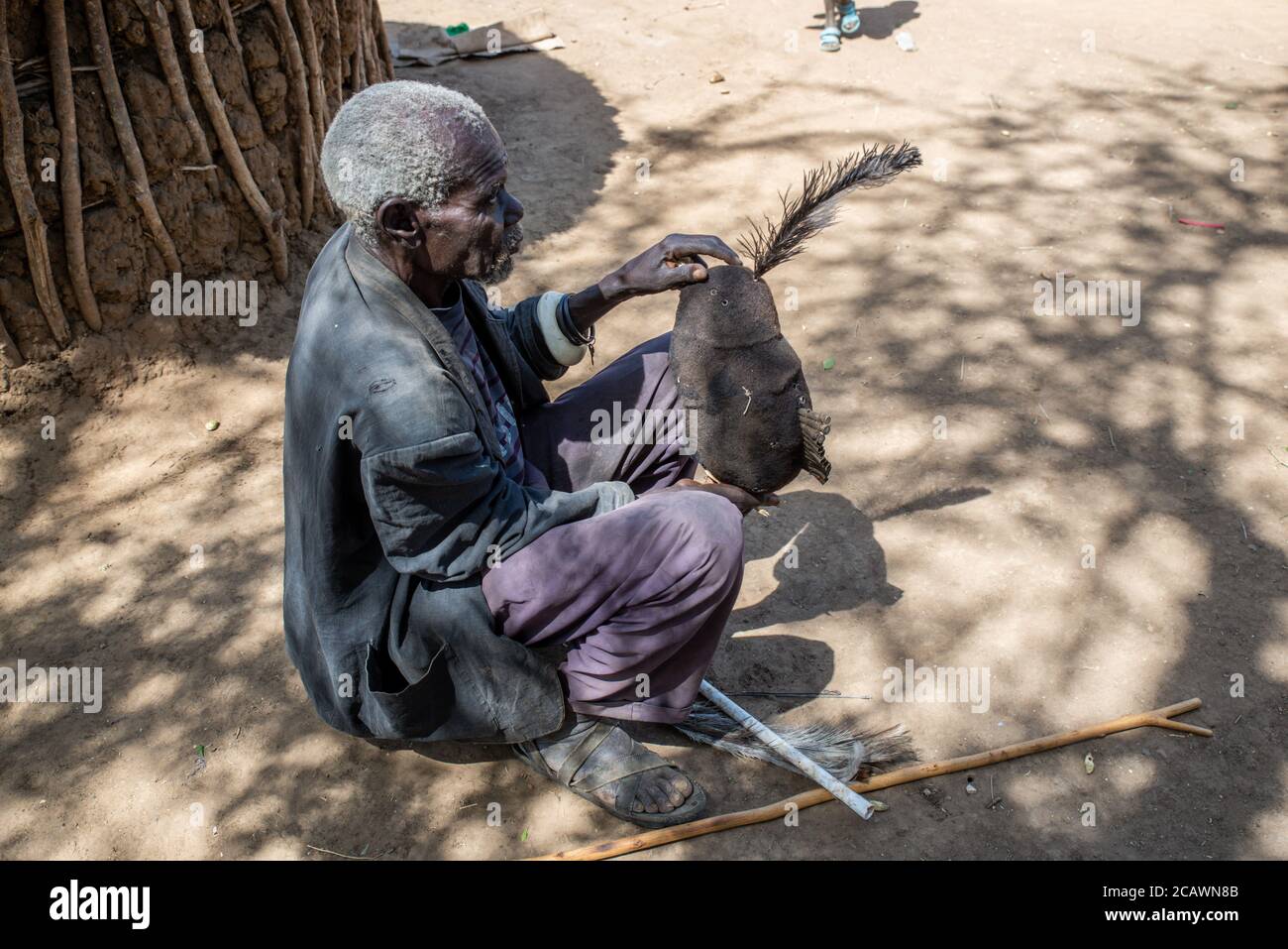 Vecchio uomo Karamejong mantenendo un hdeaddress etimat (epukot) fatto di capelli umani e piume di struzzo, distretto di Moroto, Uganda Foto Stock