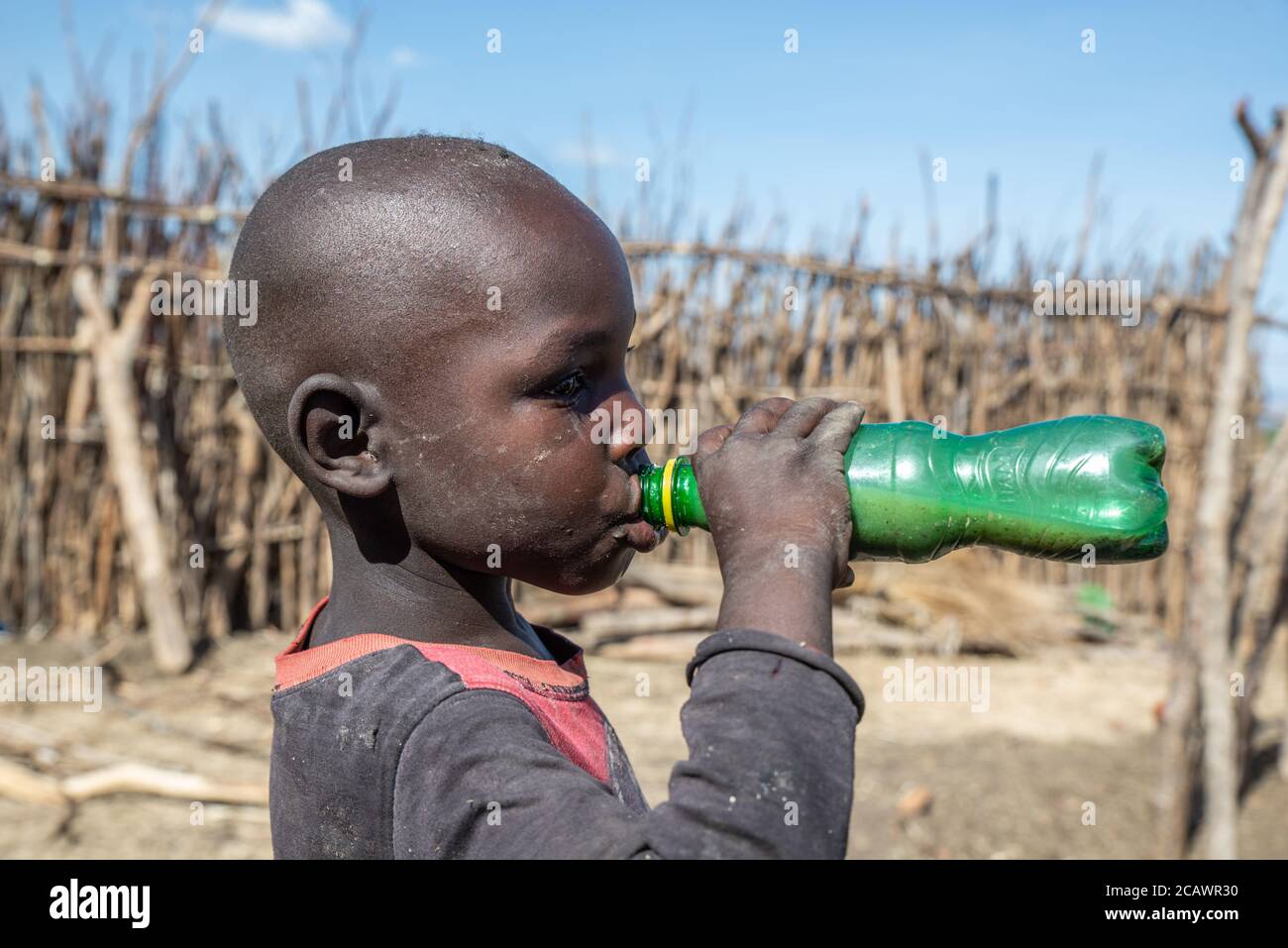 Giovane ragazzo Karamojong che beve birra a casa in un villaggio rurale, distretto di Moroto, Uganda Foto Stock