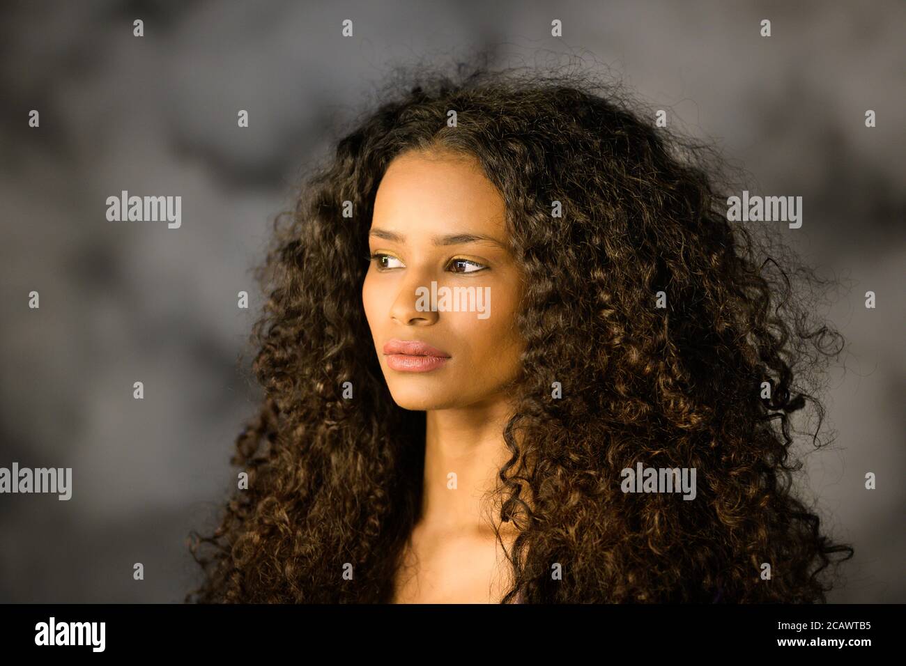 Headshot di una bella ragazza nera pensabile con lungo ricciolo capelli che guardano fuori al lato con un serio pensivo espressione Foto Stock