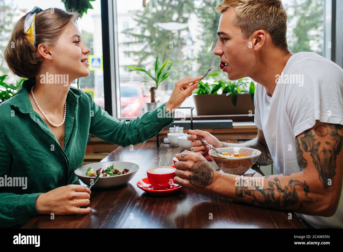 Uomo con donna in data in un caffè, gli sta dando un morso del suo pasto. Foto Stock