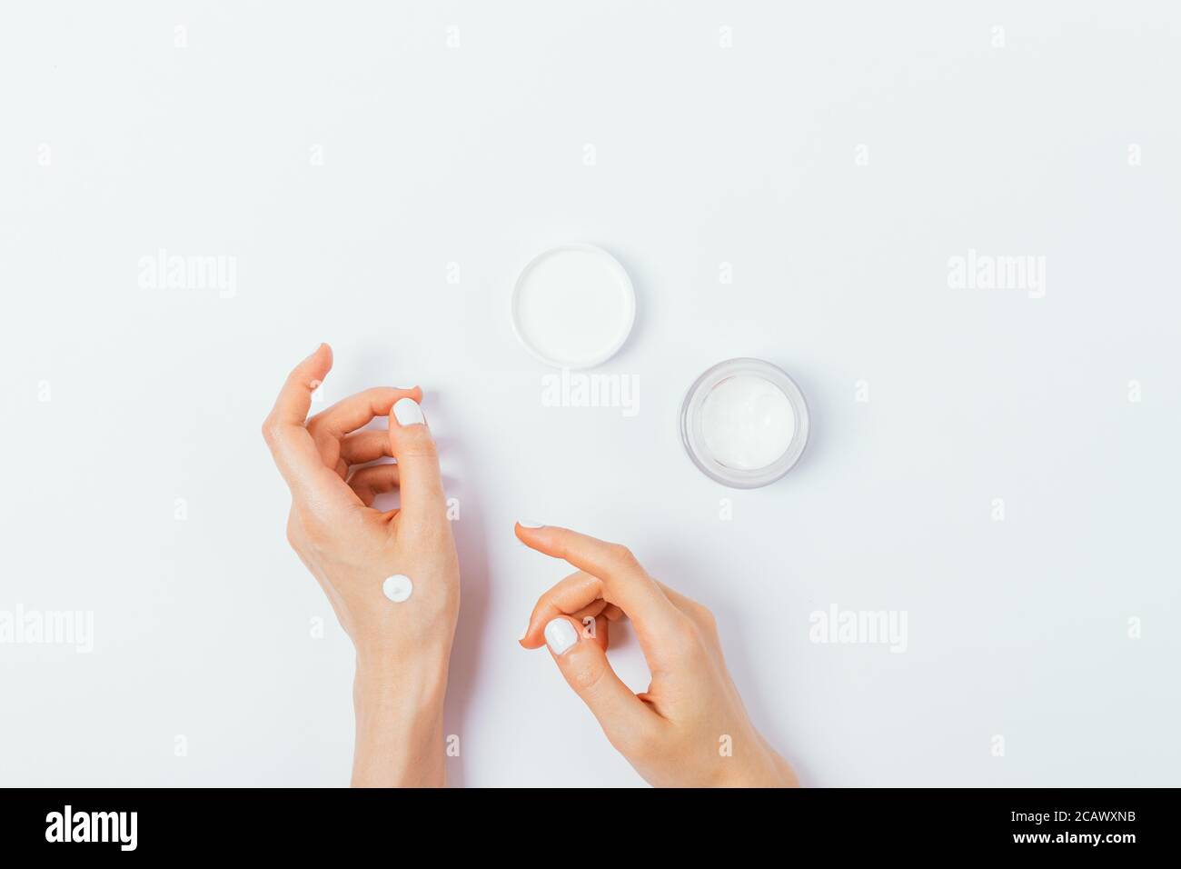 Belle mani di giovane donna con manicure applicare crema cosmetica su tavola bianca, composizione piatta. Foto Stock