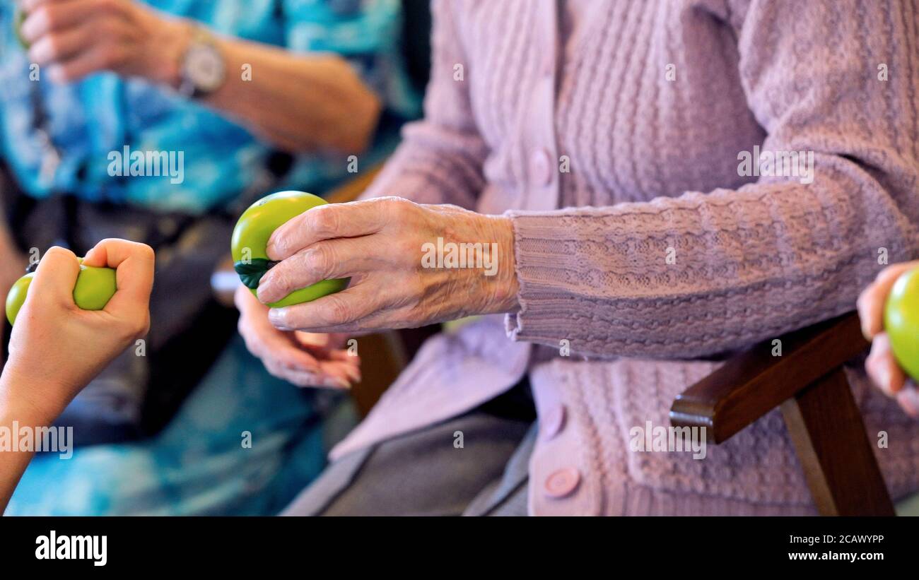 Una persona anziana che fa le esercitazioni della mano con una sfera verde di terapia. Foto Stock