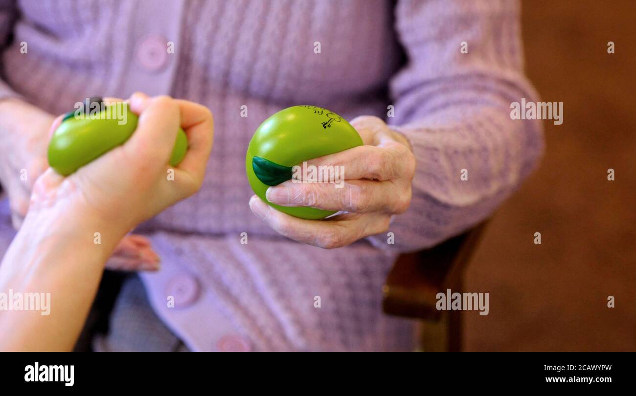 Una persona elegerly che fa le esercitazioni della mano con una sfera di terapia verde. Foto Stock
