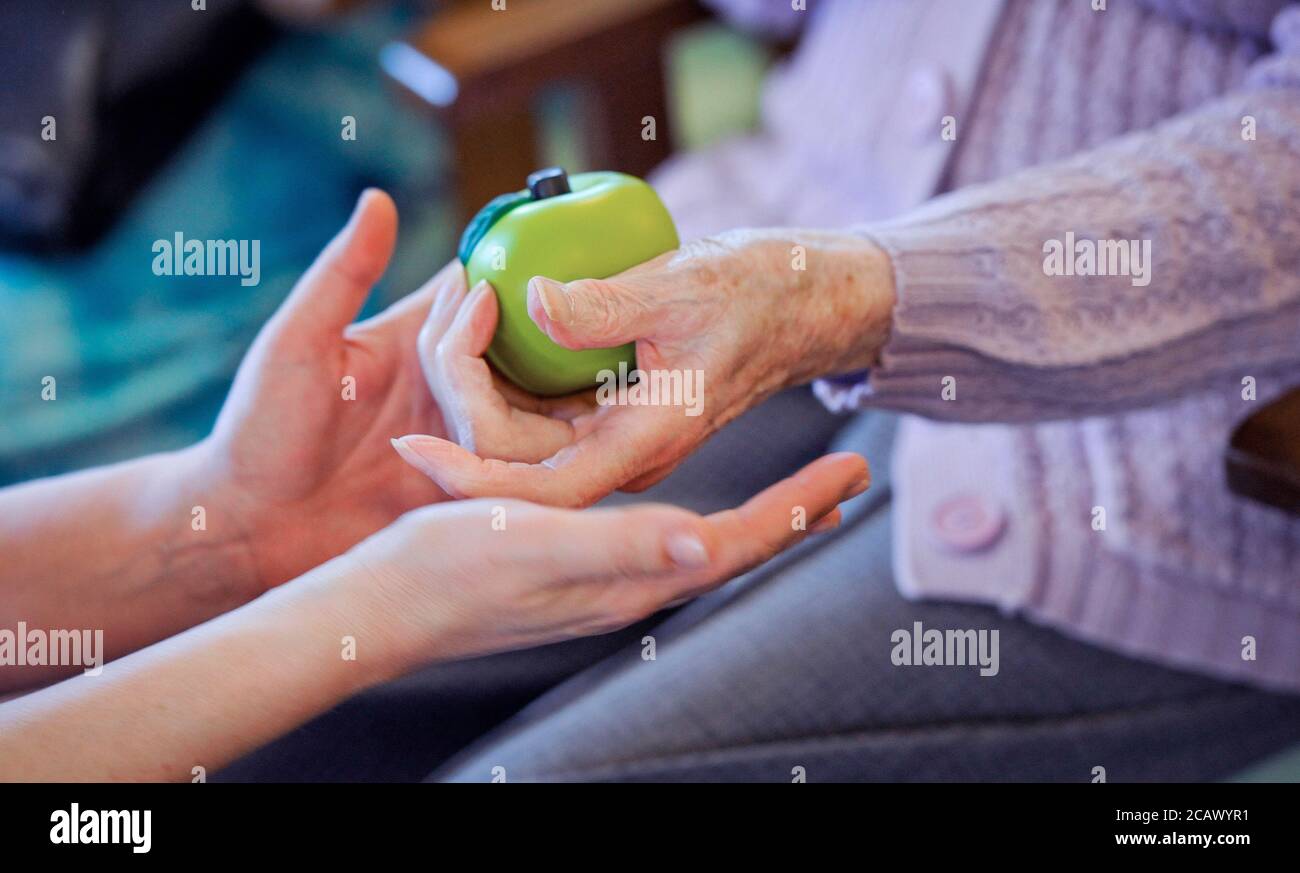 Una persona anziana che fa le esercitazioni della mano con una sfera verde di terapia. Foto Stock