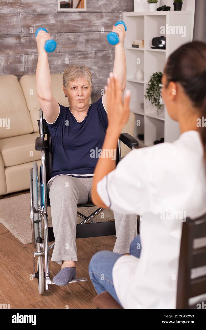 Infermiera che spiega gli esercizi di manubri per la donna anziana disabile. Anziano handicappato ricuperando l'infermiera di aiuto professionale, trattamento di pensione di cura e riabilitazione Foto Stock