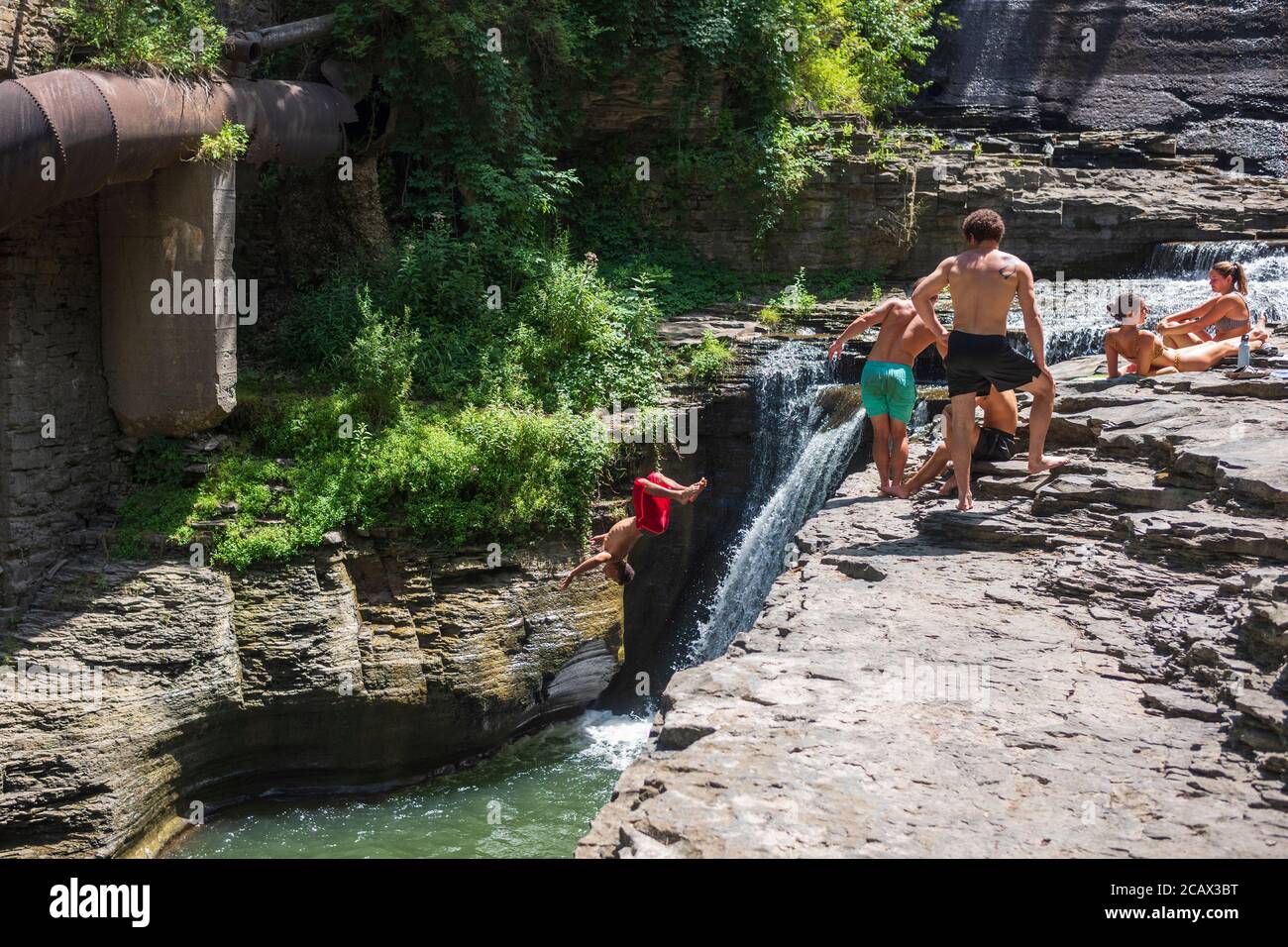Ithaca, NY-USA / 2 agosto 2020: Un giovane salta da una scogliera in una piscina naturale di acqua a Six-Mile Creek. Molti si affollano di parchi per sfuggire l'estate h Foto Stock