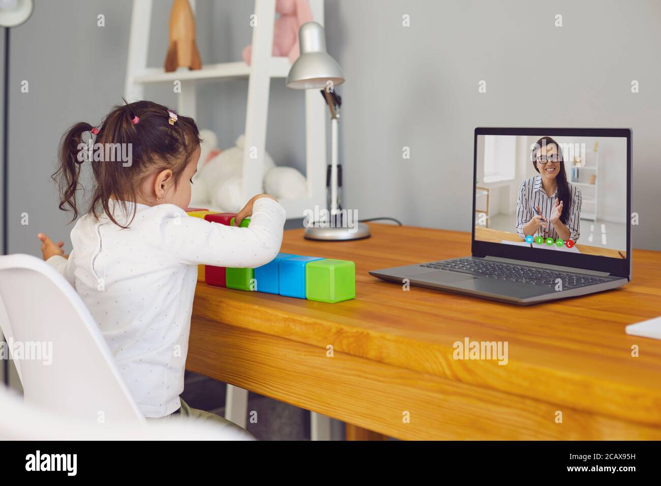 Insegnante educatore insegna il bambino online. Un bambino fa una lezione seduto a un tavolo usando un laptop a casa da remoto. Foto Stock