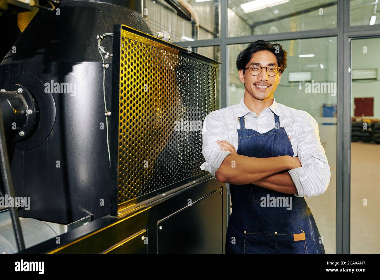 Ritratto di un uomo allegro e fiducioso che sorride in piedi al caffè roaster e sorridendo alla macchina fotografica Foto Stock