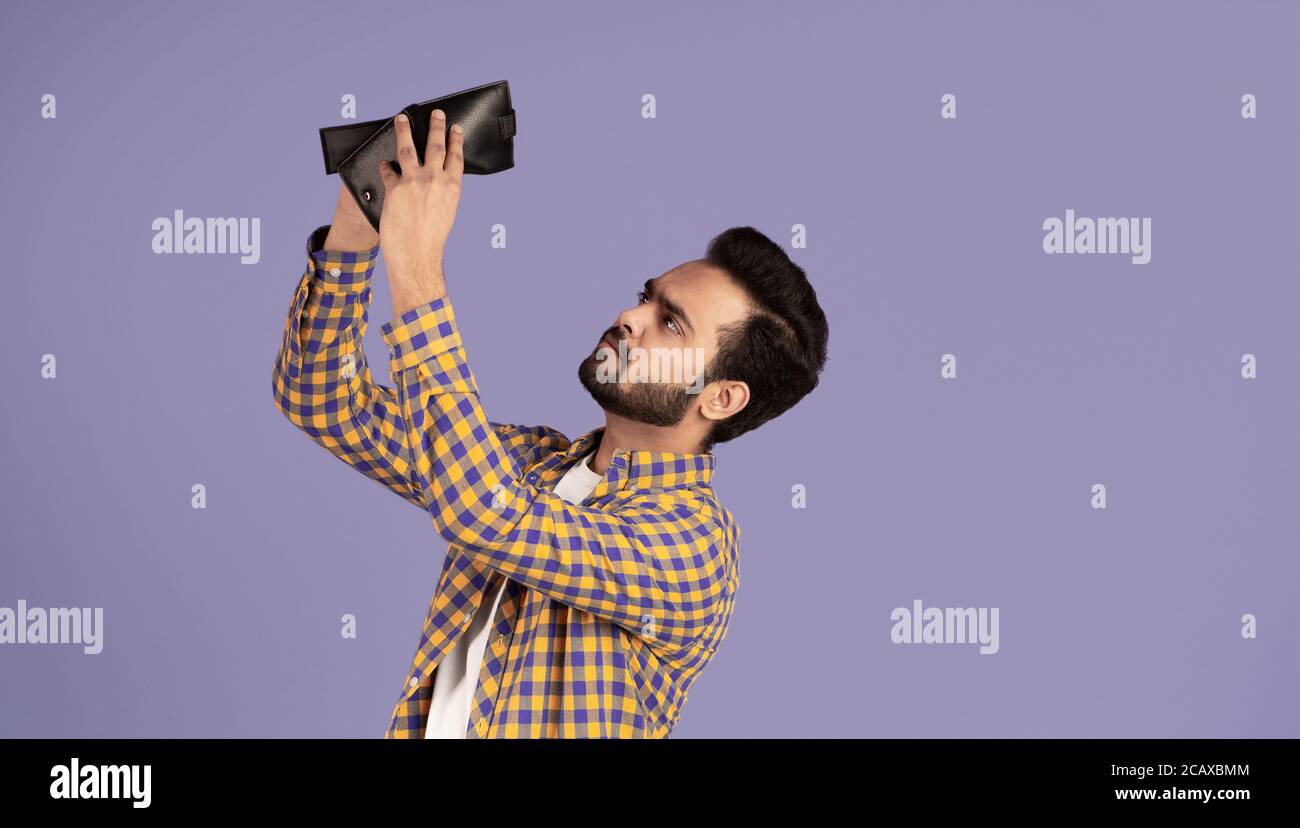 Concetto di crisi economica. Un ragazzo indiano sconvolto con un portafoglio vuoto su sfondo viola Foto Stock