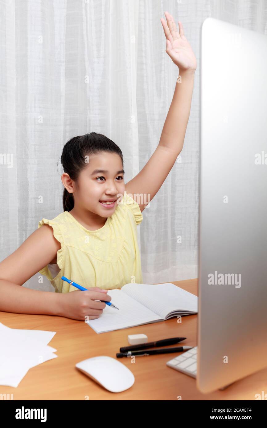 La bambina asiatica sta studiando in linea via il Internet che siede e scrive nel soggiorno a casa. Asia bambini scrivere con matita su notebook di carta Foto Stock