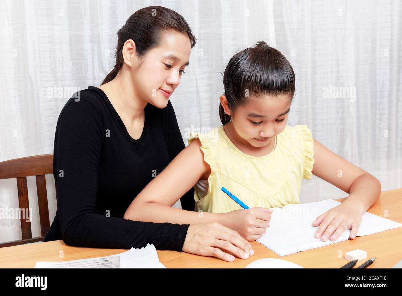 Ragazza giovane asiatica che usa la matita per fare i compiti con la madre. Libro di scrittura del capretto dello studente. La ragazza usa il computer per studiare a casa. Istruzione Foto Stock