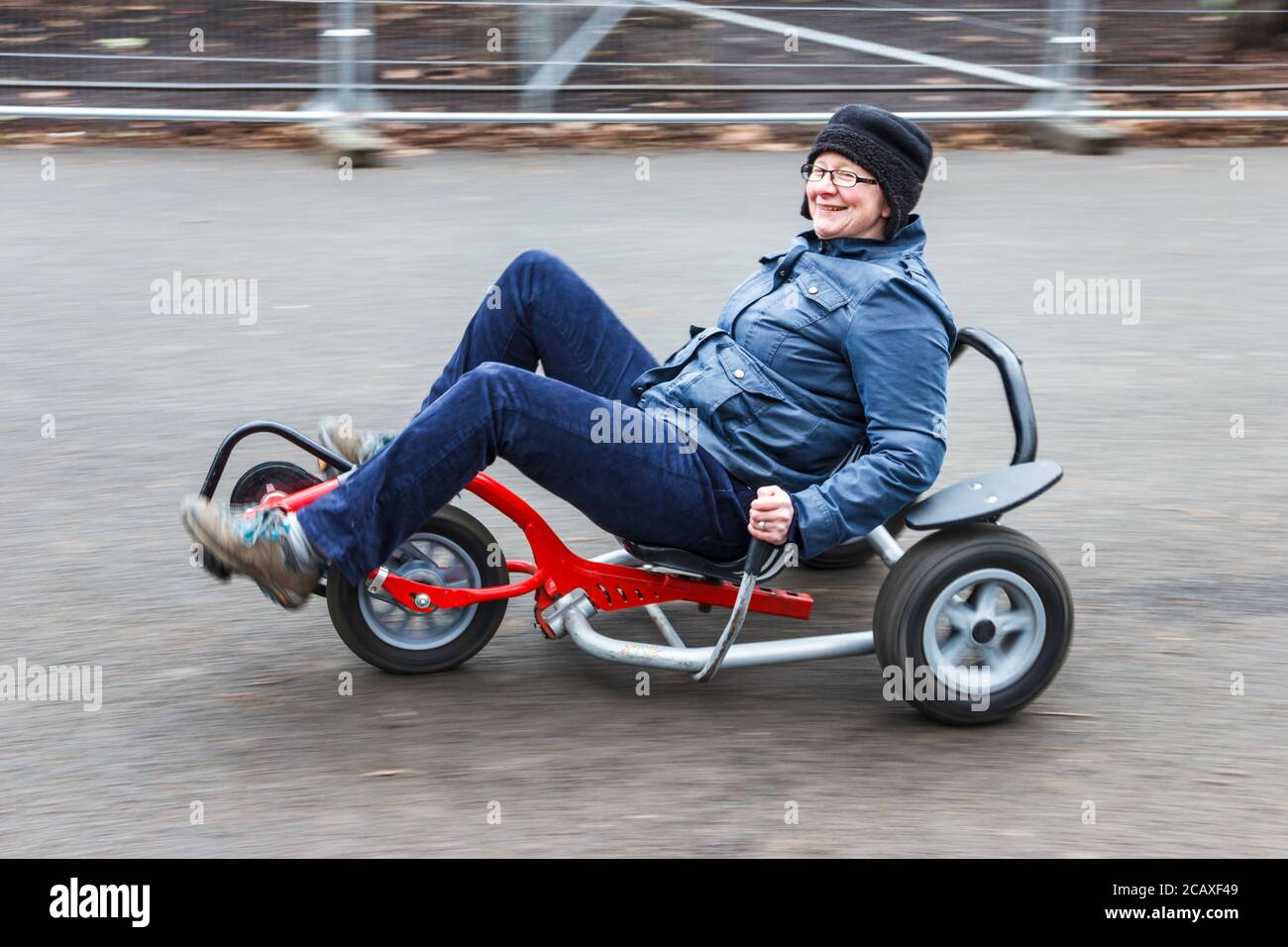 Sorridente donna di mezza età che si gode un giro su un triciclo recumbent go-kart, Londra, Regno Unito Foto Stock