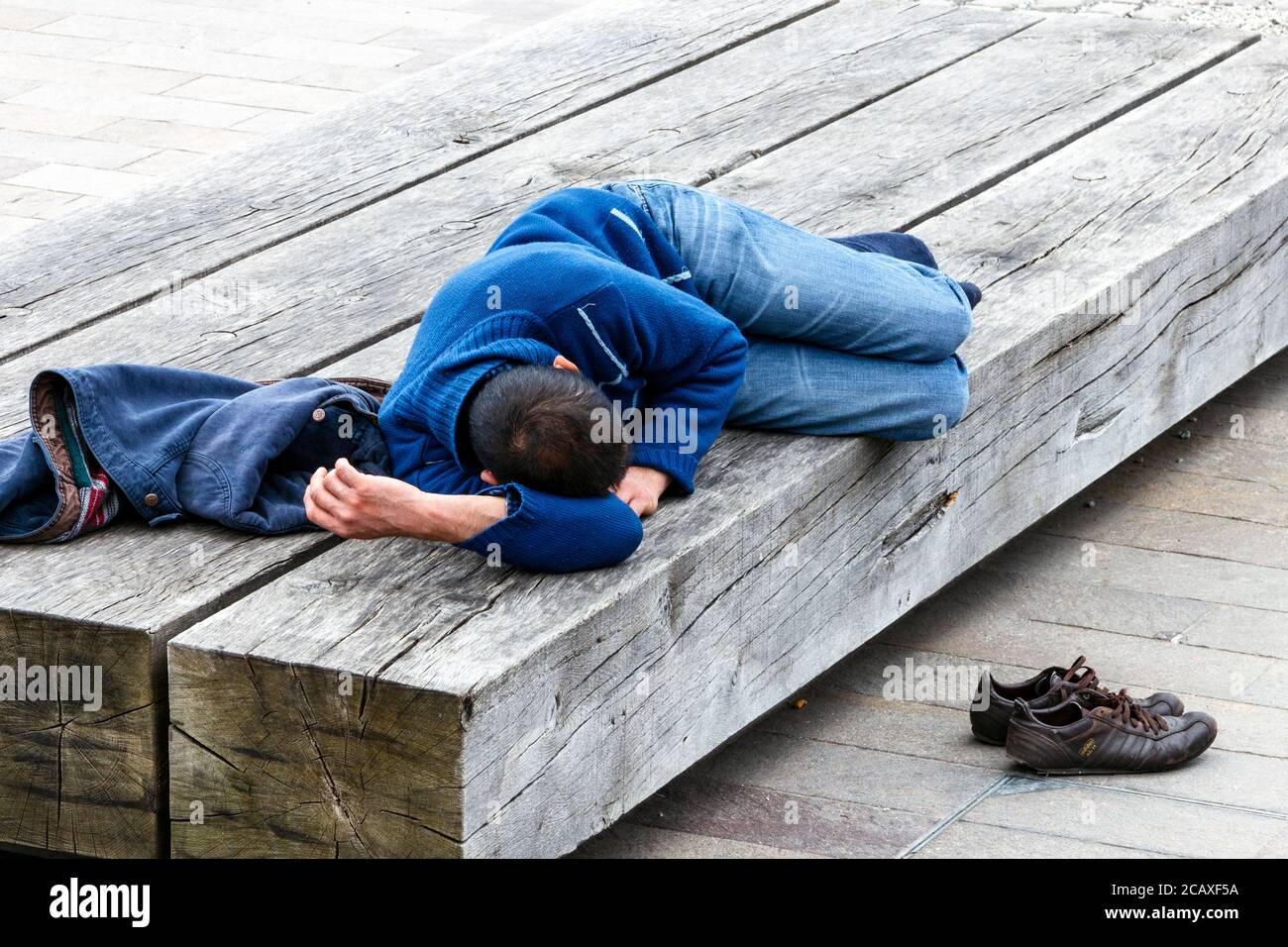 Un giovane che prende un pisolino pomeridiano su una panchina di legno a King's Cross, Londra, Regno Unito Foto Stock