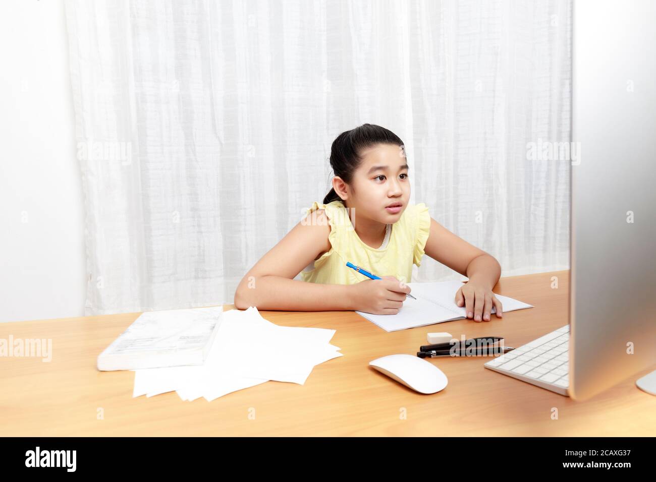 Ragazza giovane asiatica che usa la matita per fare i compiti da sola. Libro di scrittura del capretto dello studente. La ragazza usa il computer per studiare a casa. Istruzione a casa Foto Stock